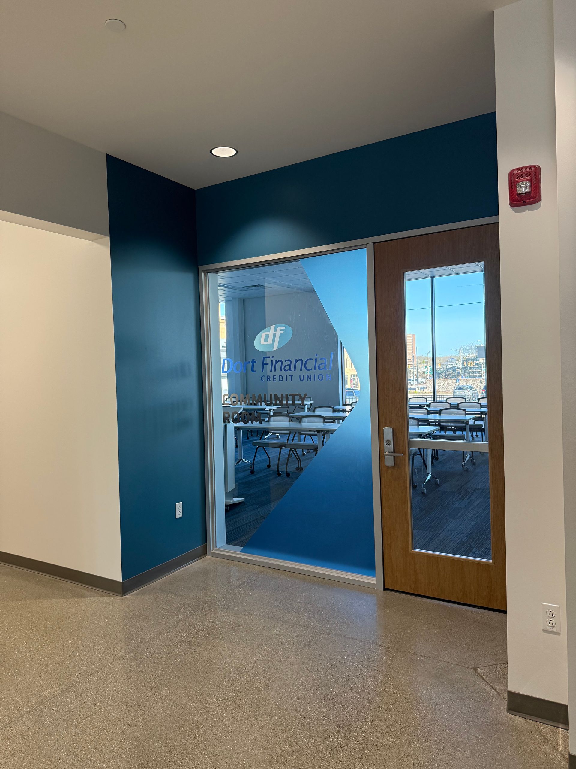 A hallway with a glass door and a fire extinguisher on the wall.