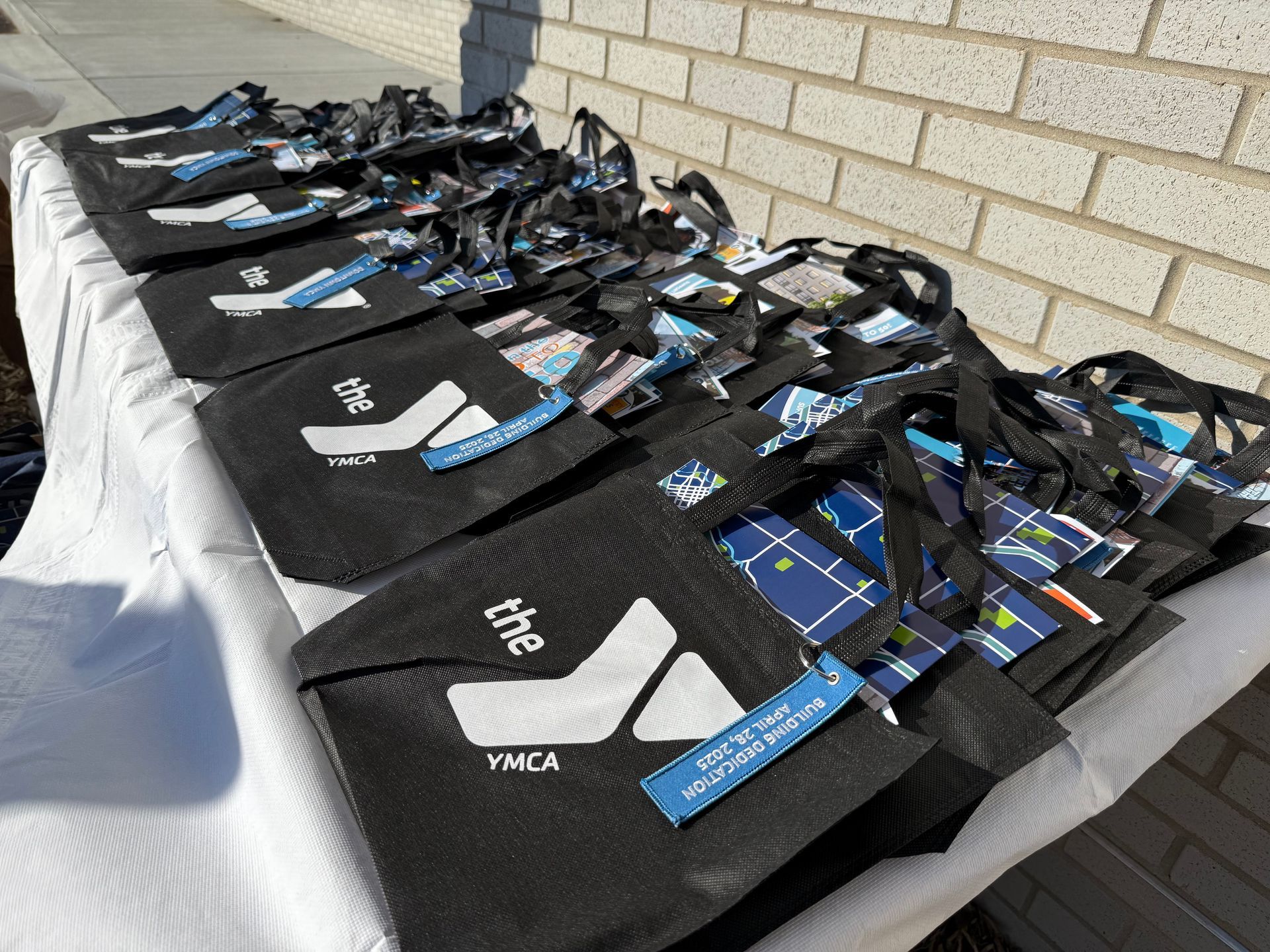 A row of black bags with the ymca logo on them are lined up on a table.
