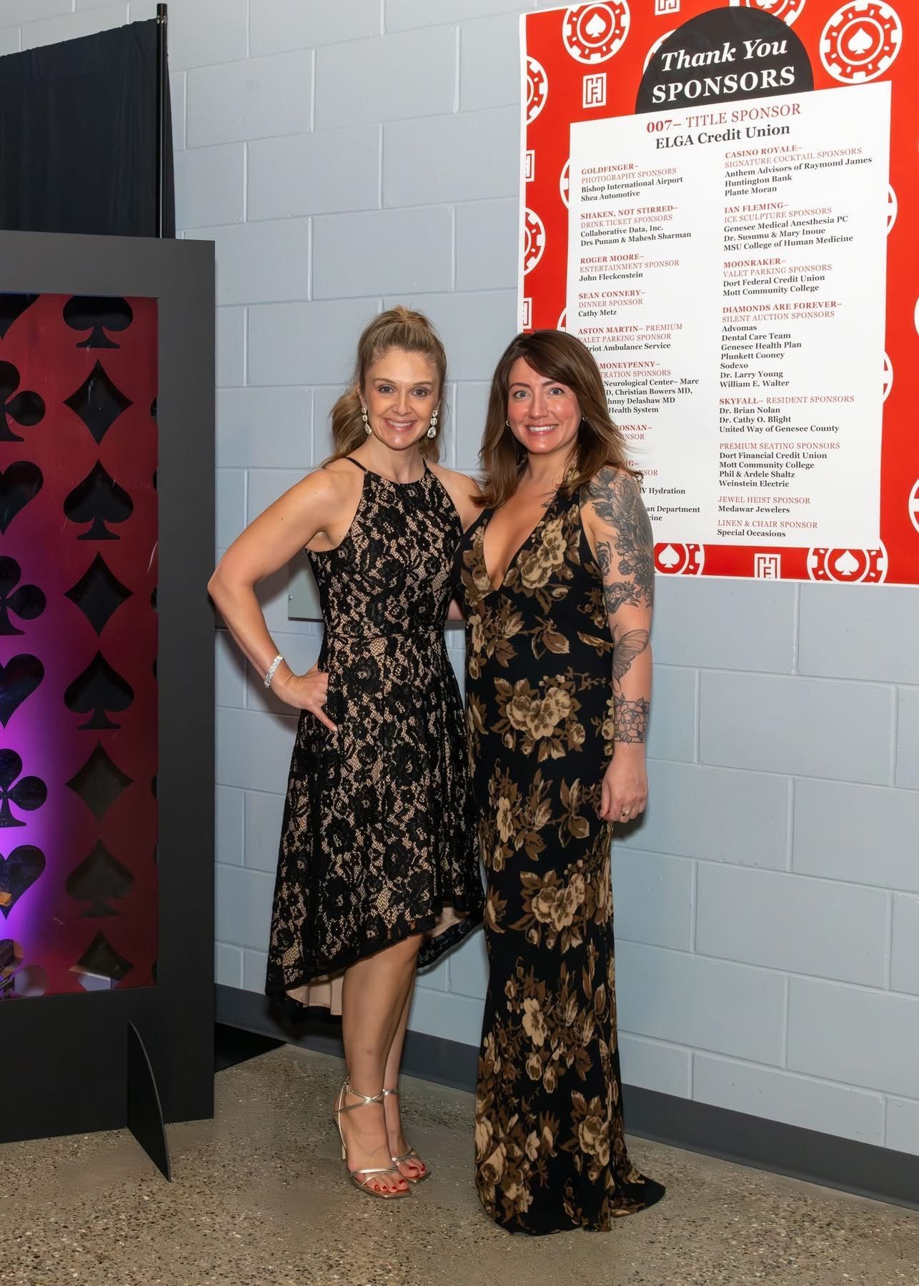 Two women are standing next to each other in front of a brick wall.