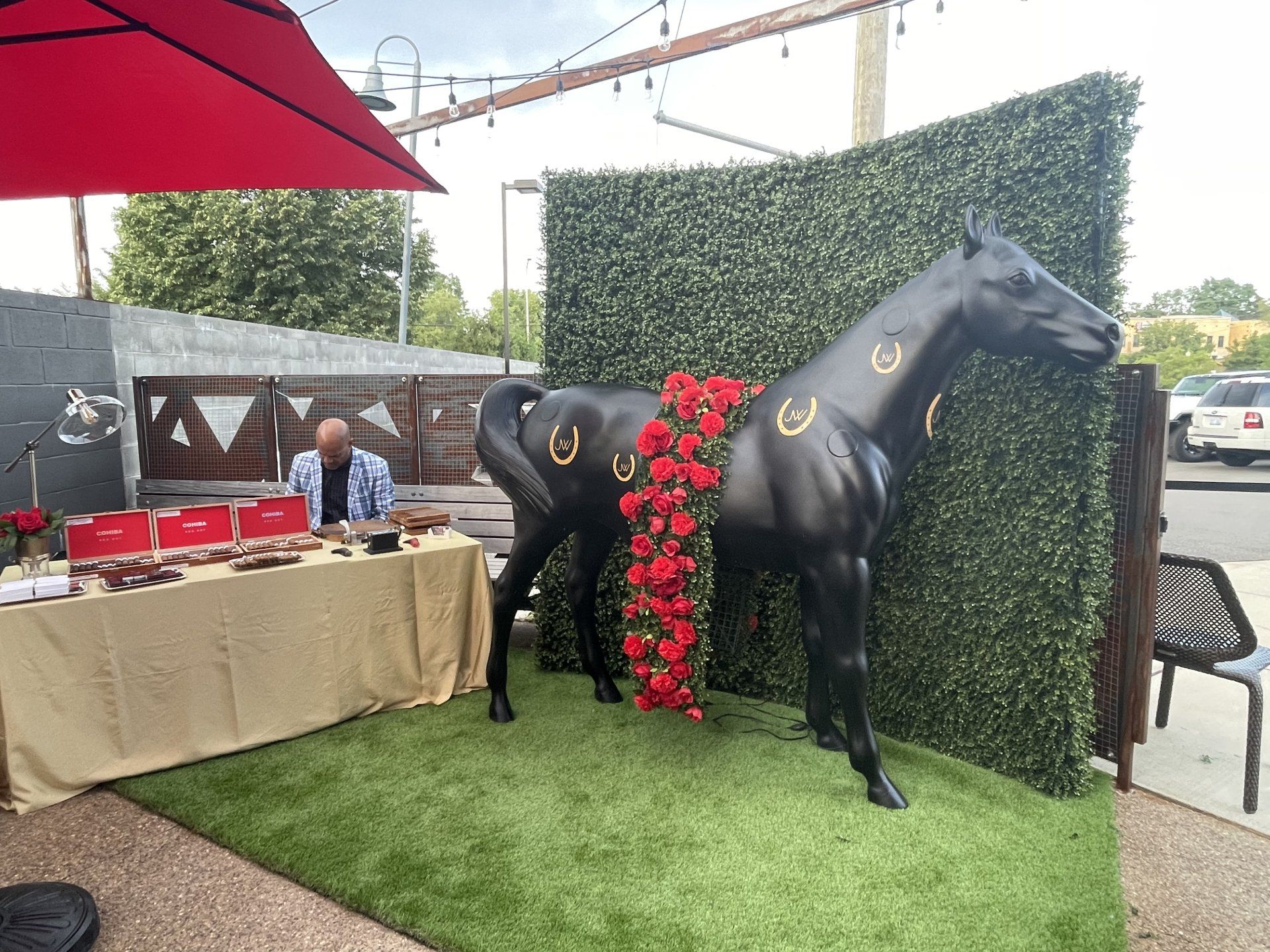 A man is sitting at a table under an umbrella next to a statue of a horse.