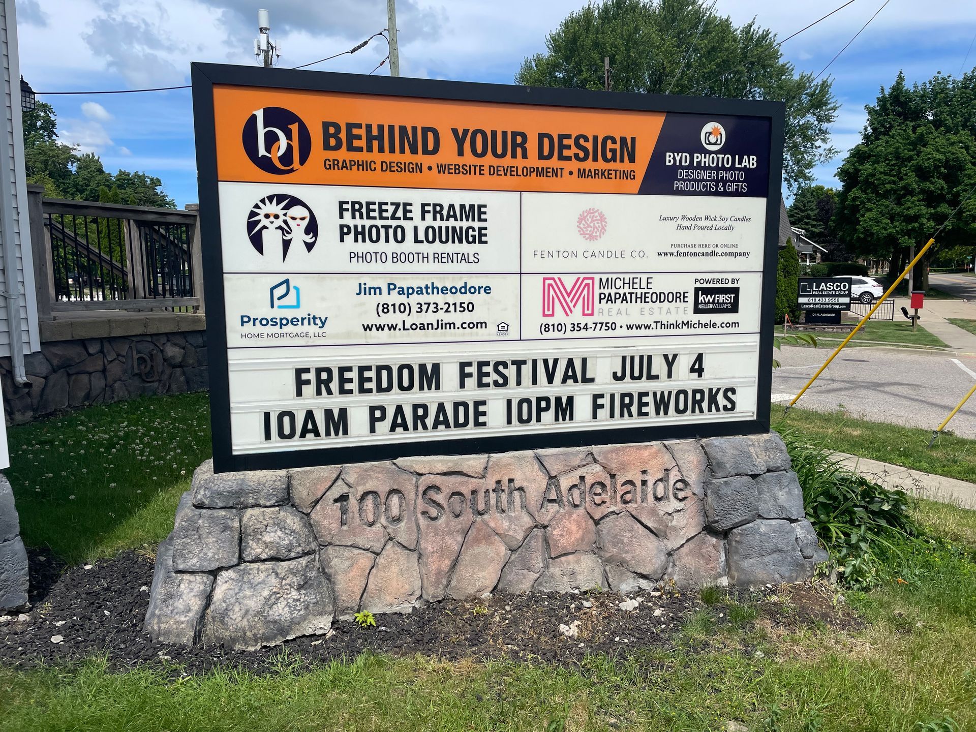Outdoor sign for Behind Your Design event, with sponsor logos and “Laff Paddle & Pedal” details on stone base