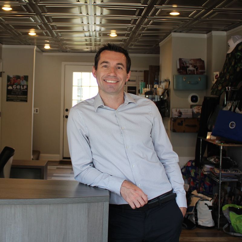 A man in a light blue shirt is leaning on a counter and smiling