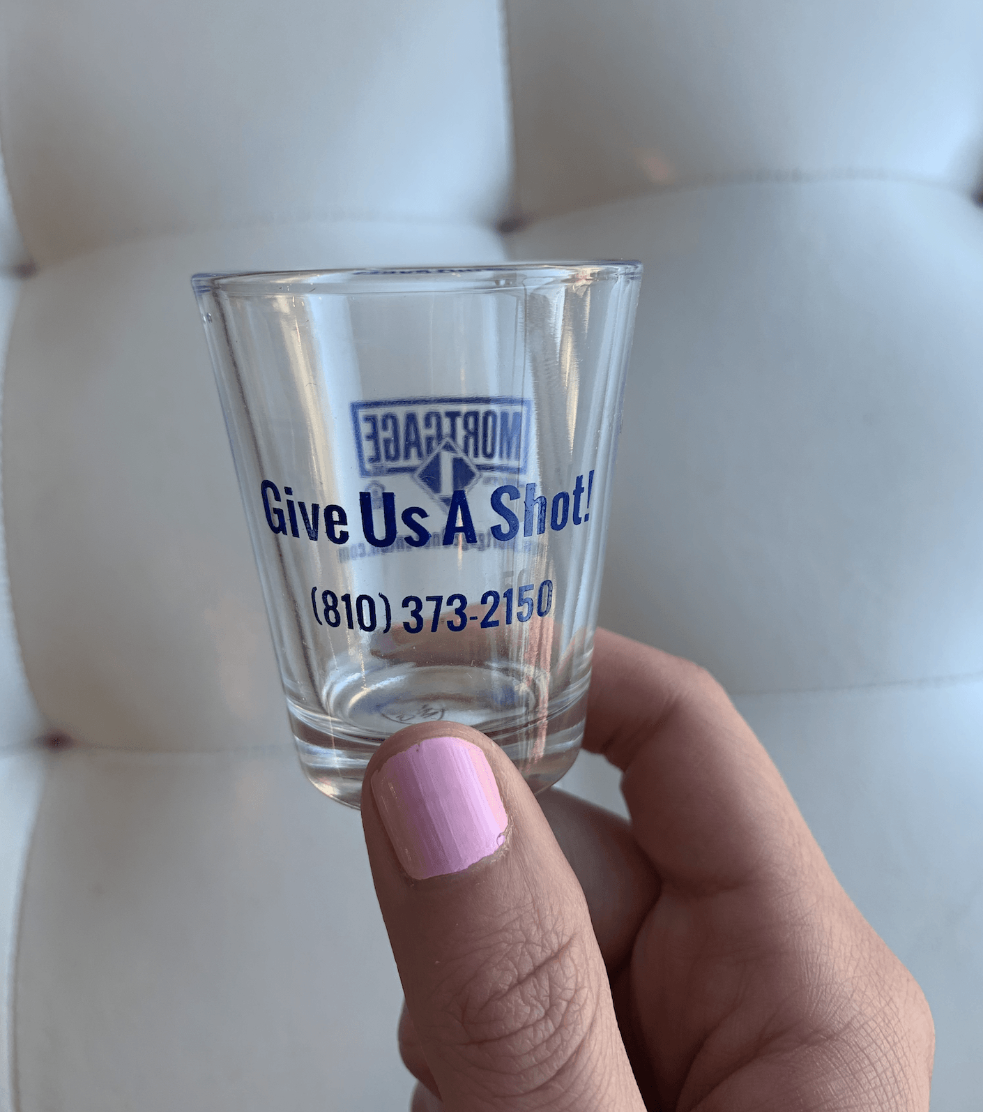 A person is holding a shot glass that says give us a shot.