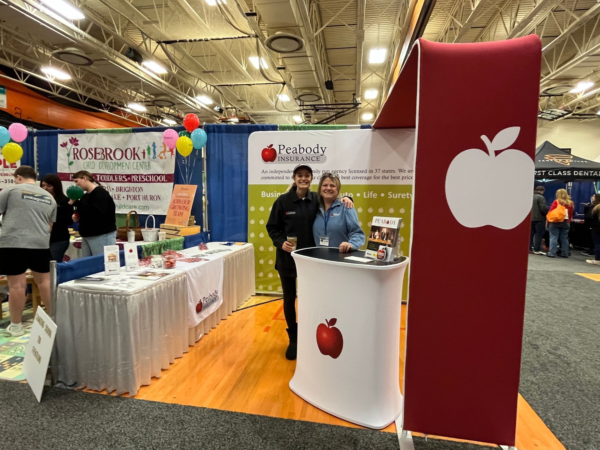 A man and a woman are standing in front of a booth at a convention.