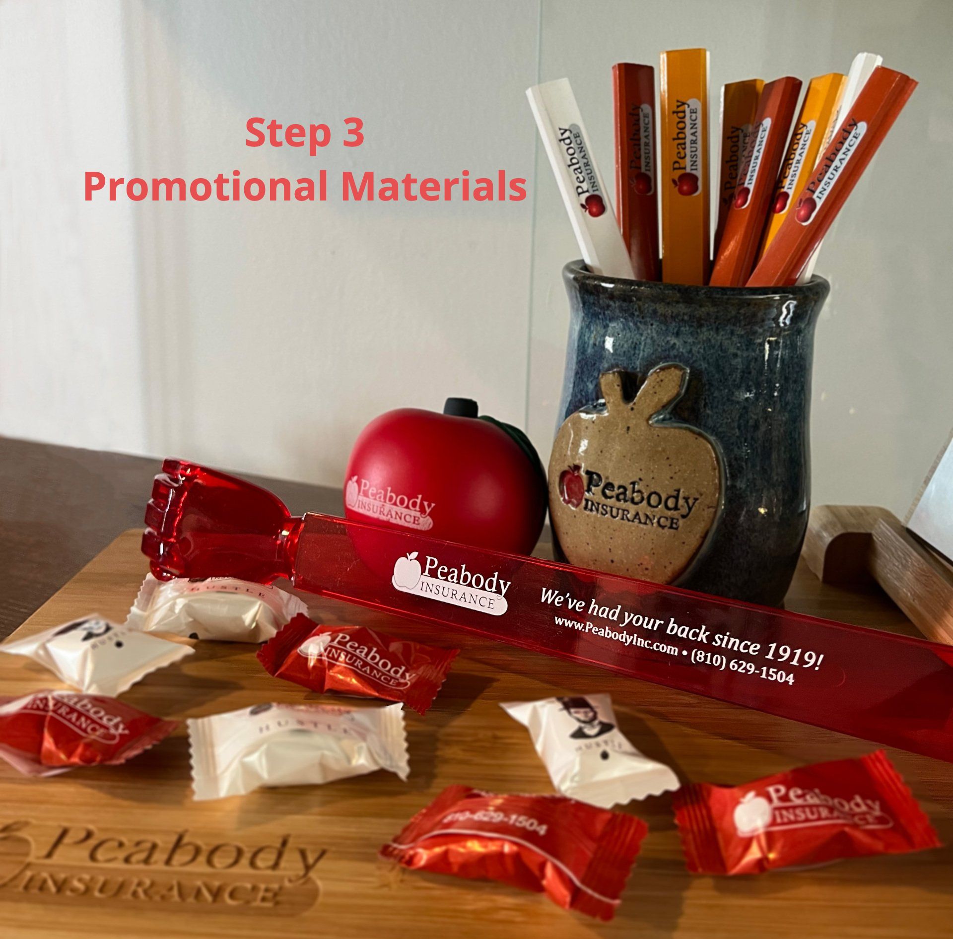 Promotional items including pencils, backscratchers, mints, mug, charcuterie board  and apple shaped stressball with the Peabody Insurance, Fenton MI, logo