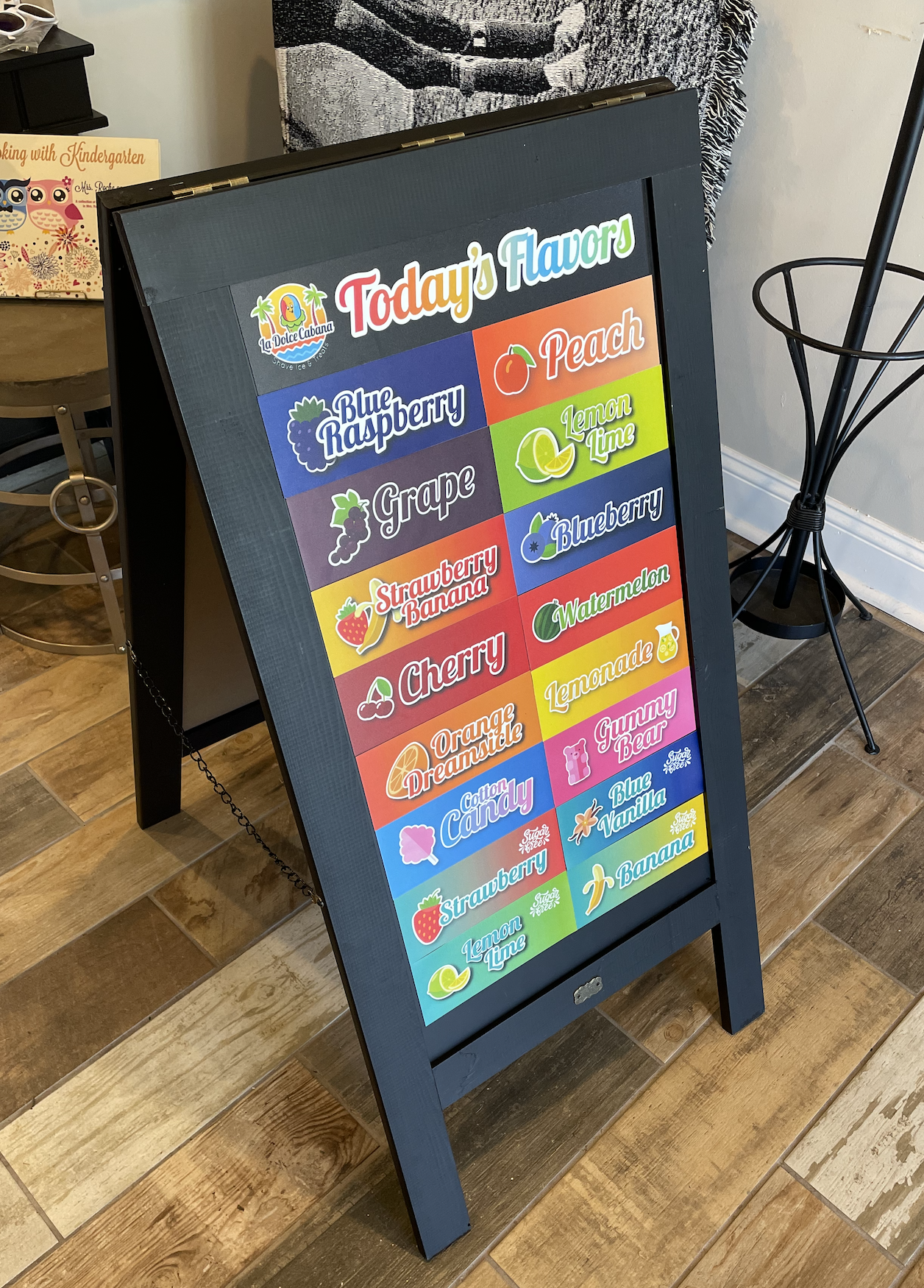A chalkboard with a variety of fruits and vegetables on it is sitting on a wooden floor.