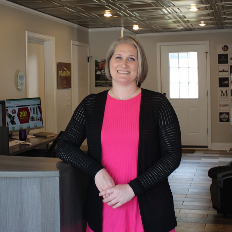 A woman in a pink dress and black cardigan stands in front of a counter