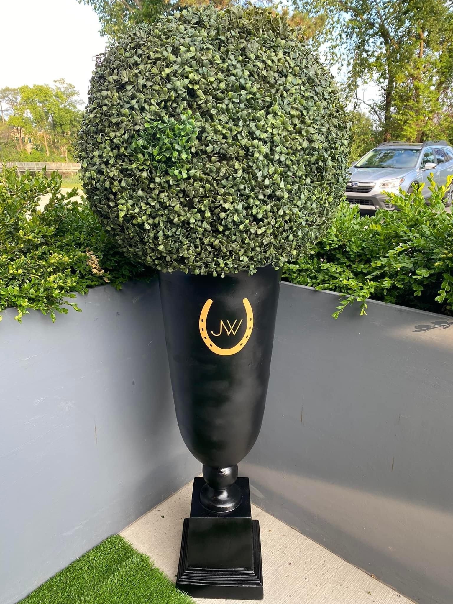 A large black vase with a horseshoe on it is sitting on top of a lush green lawn.