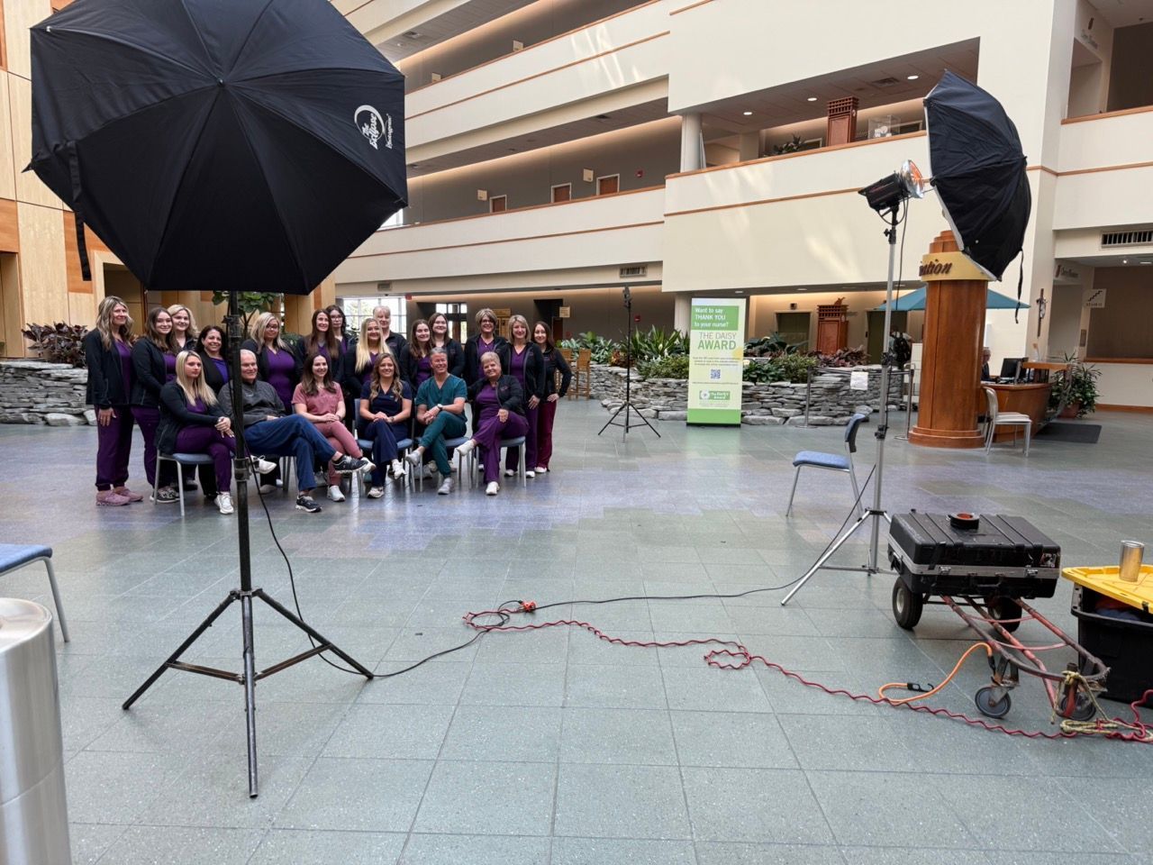 A group of people are sitting in chairs in front of a black umbrella.