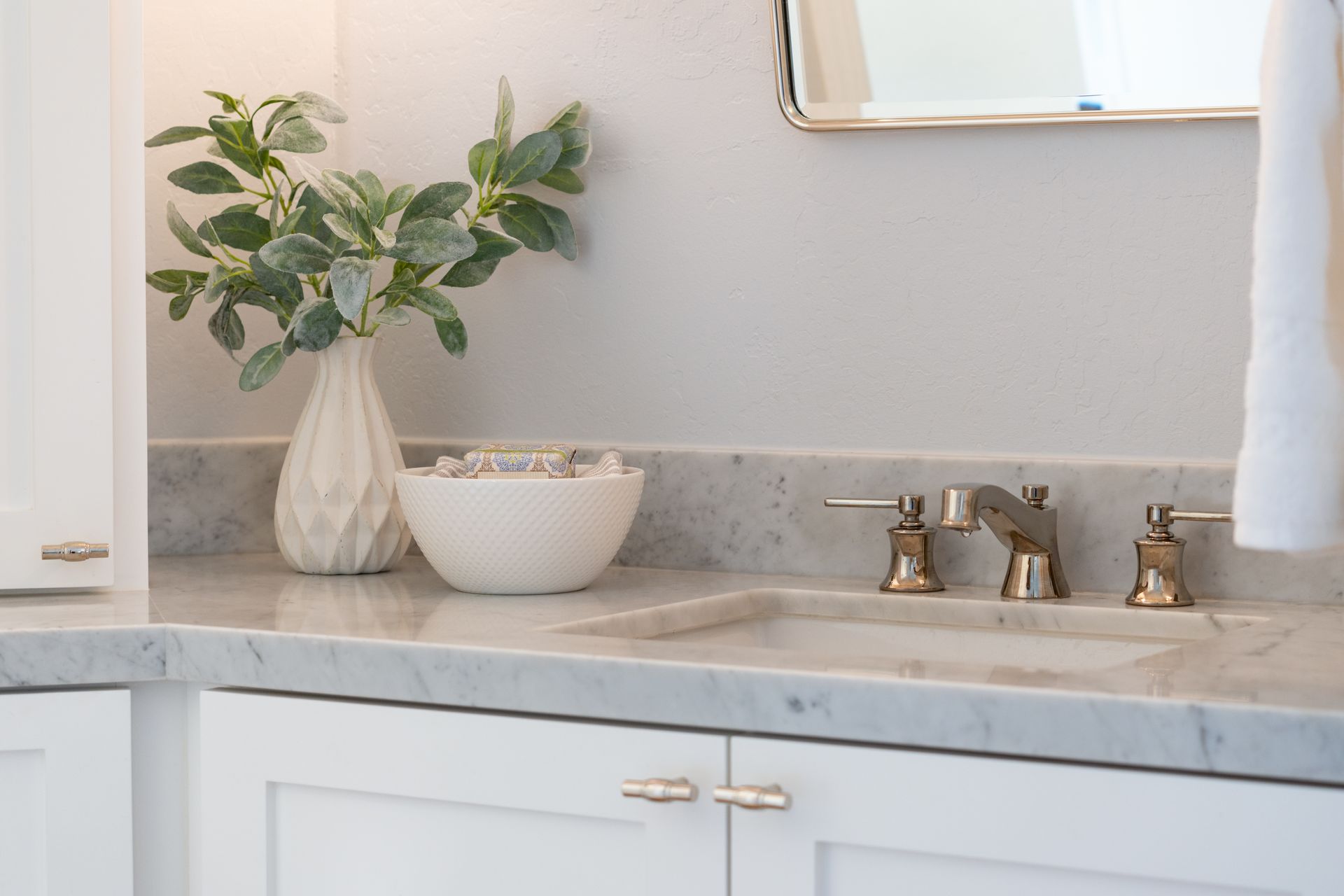 A bathroom sink with a plant in a vase on the counter.