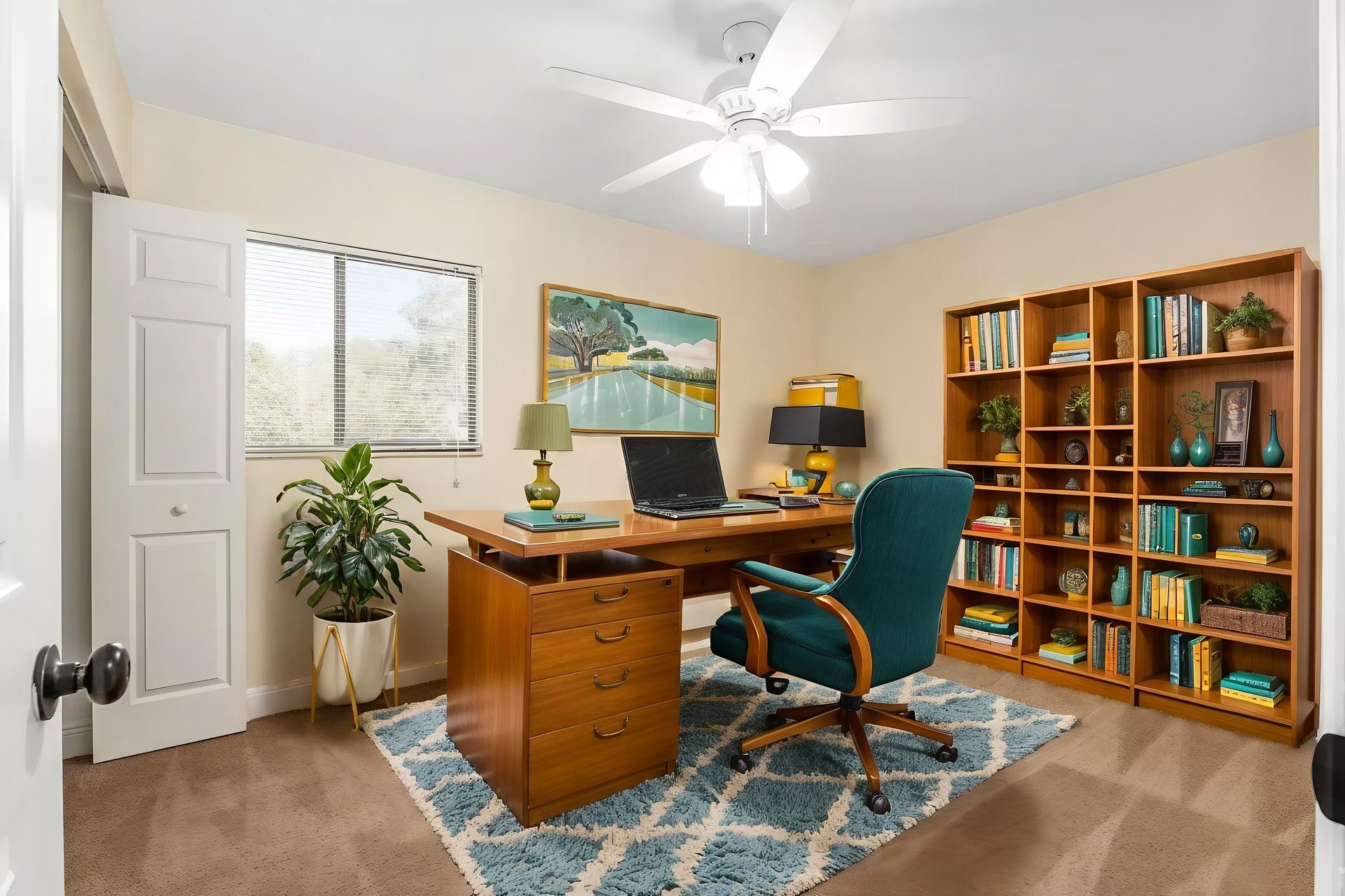 Office with desk, bookcase, teal chair, painting, indoor plant, and rug. Beige walls and carpet.