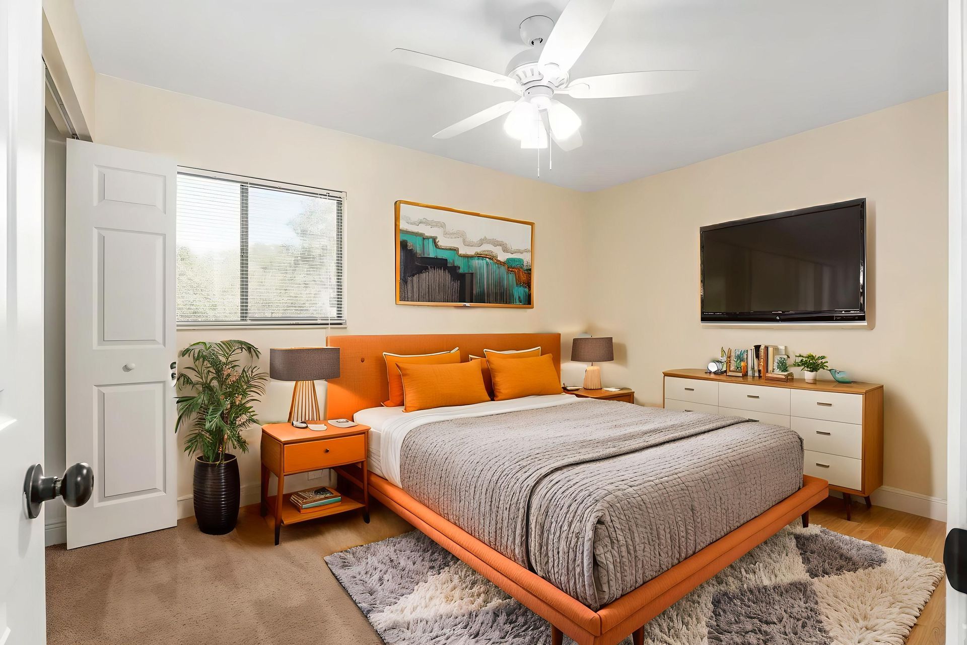 Orange-themed bedroom with bed, nightstands, dresser, tv, rug, and artwork. Light beige walls and brown carpet.