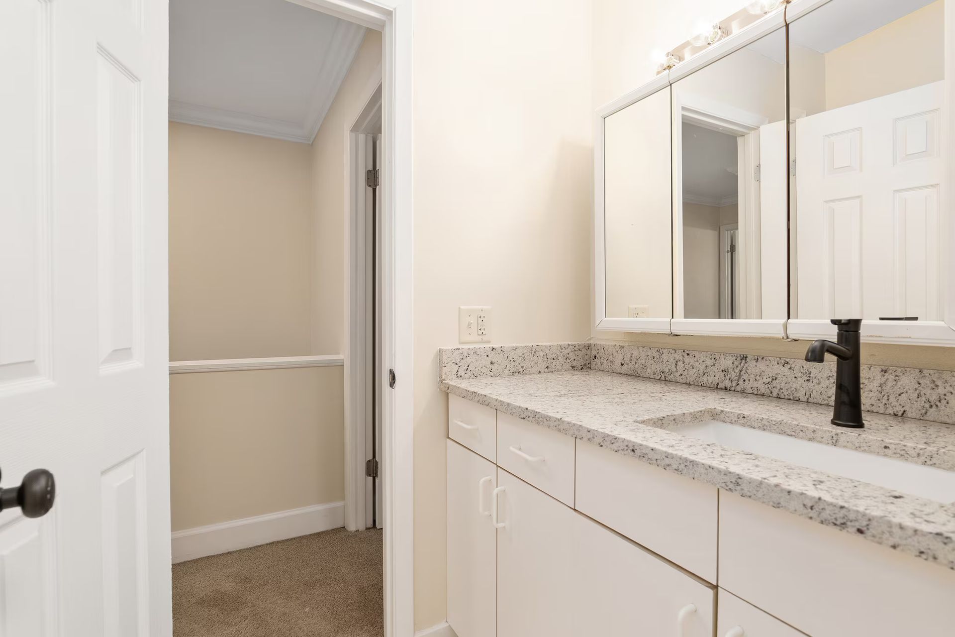 Bathroom with a white vanity, speckled countertop, and a walk-in closet.