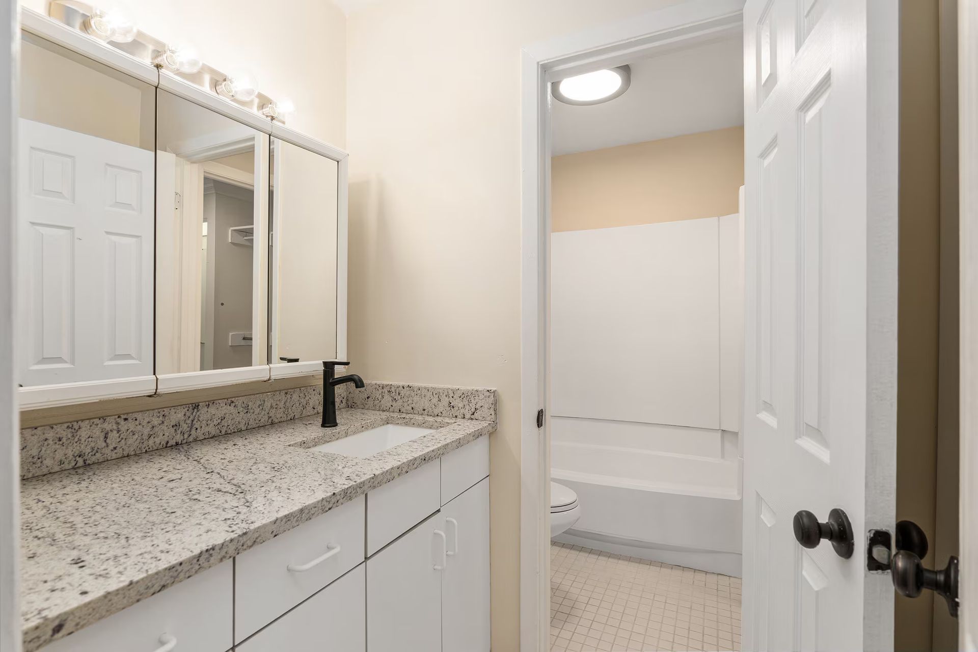Bathroom with white vanity, granite countertop, and open door to a tub/shower.