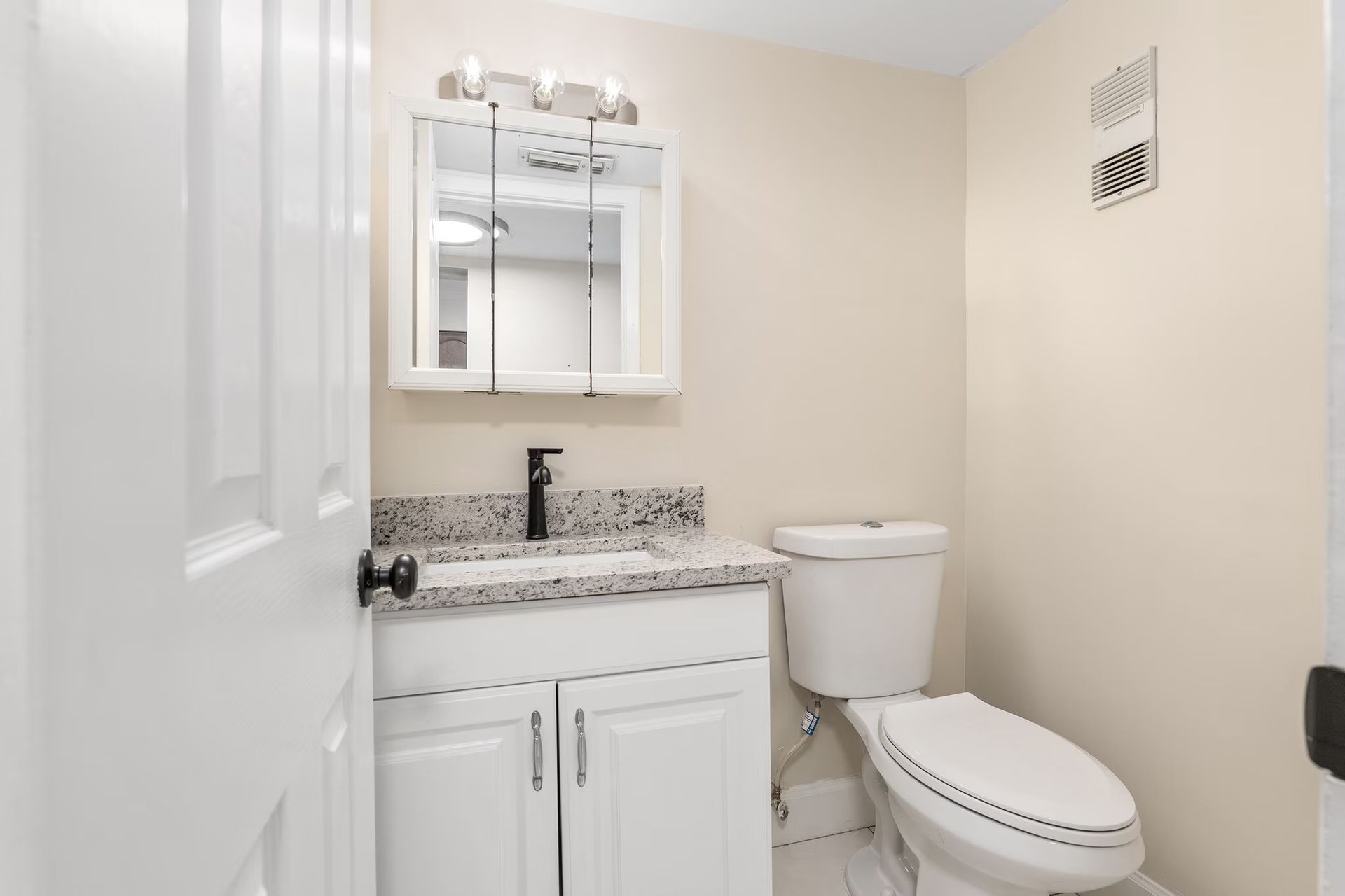 A small bathroom with a white vanity, toilet, and mirror above a sink.