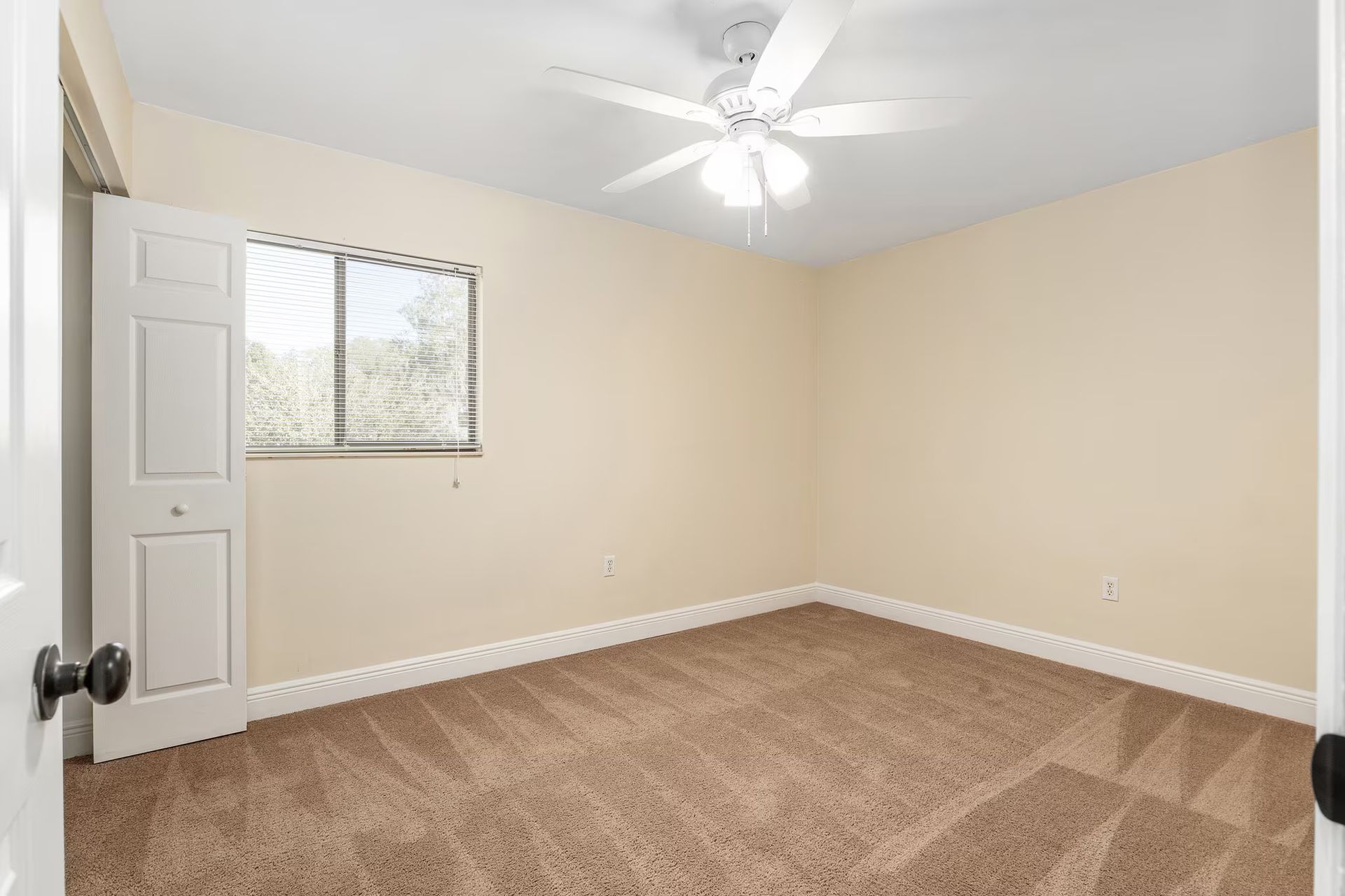 Empty beige bedroom with carpet, a window, and a ceiling fan.