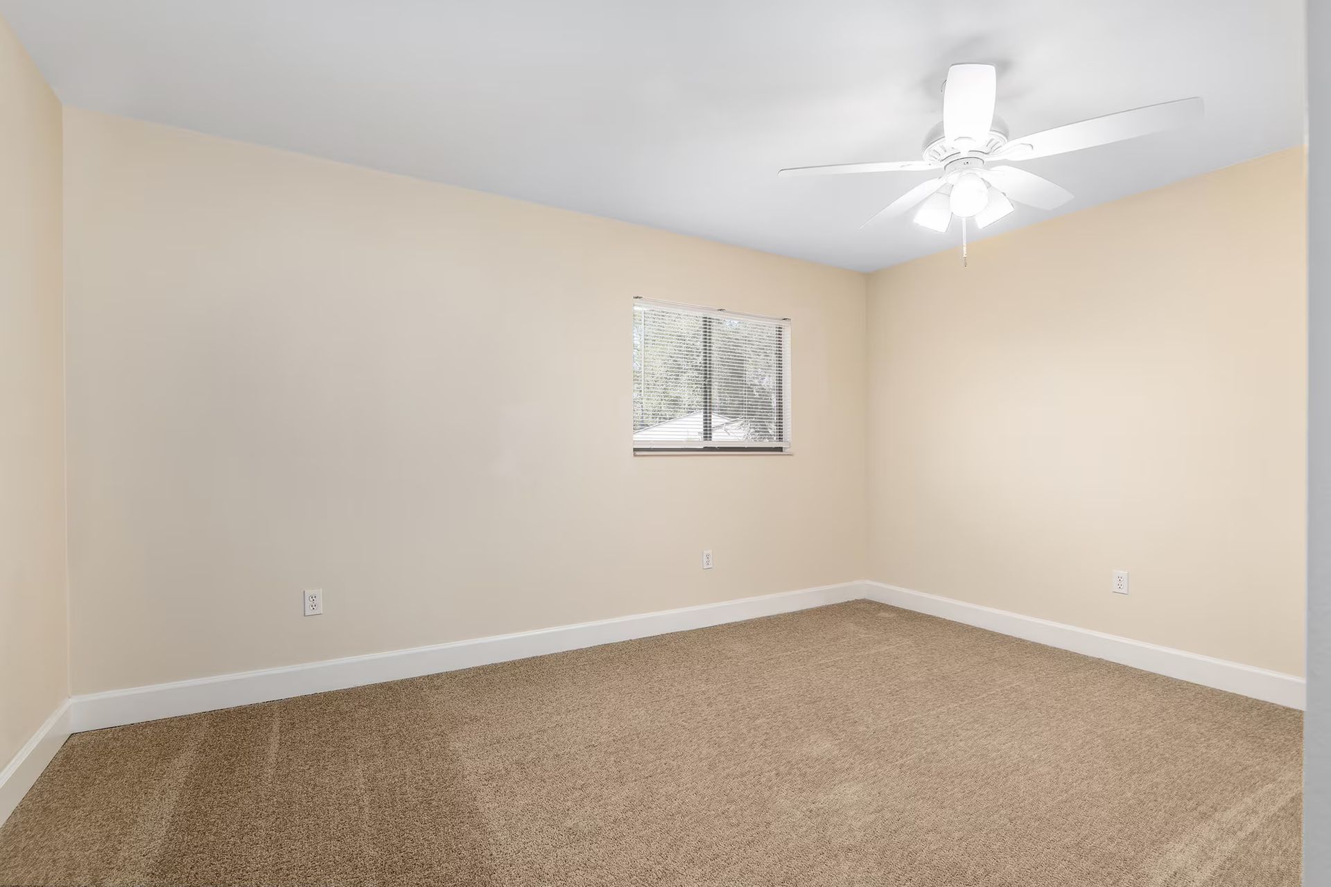 Empty bedroom with tan walls, carpet, a window, and a ceiling fan.