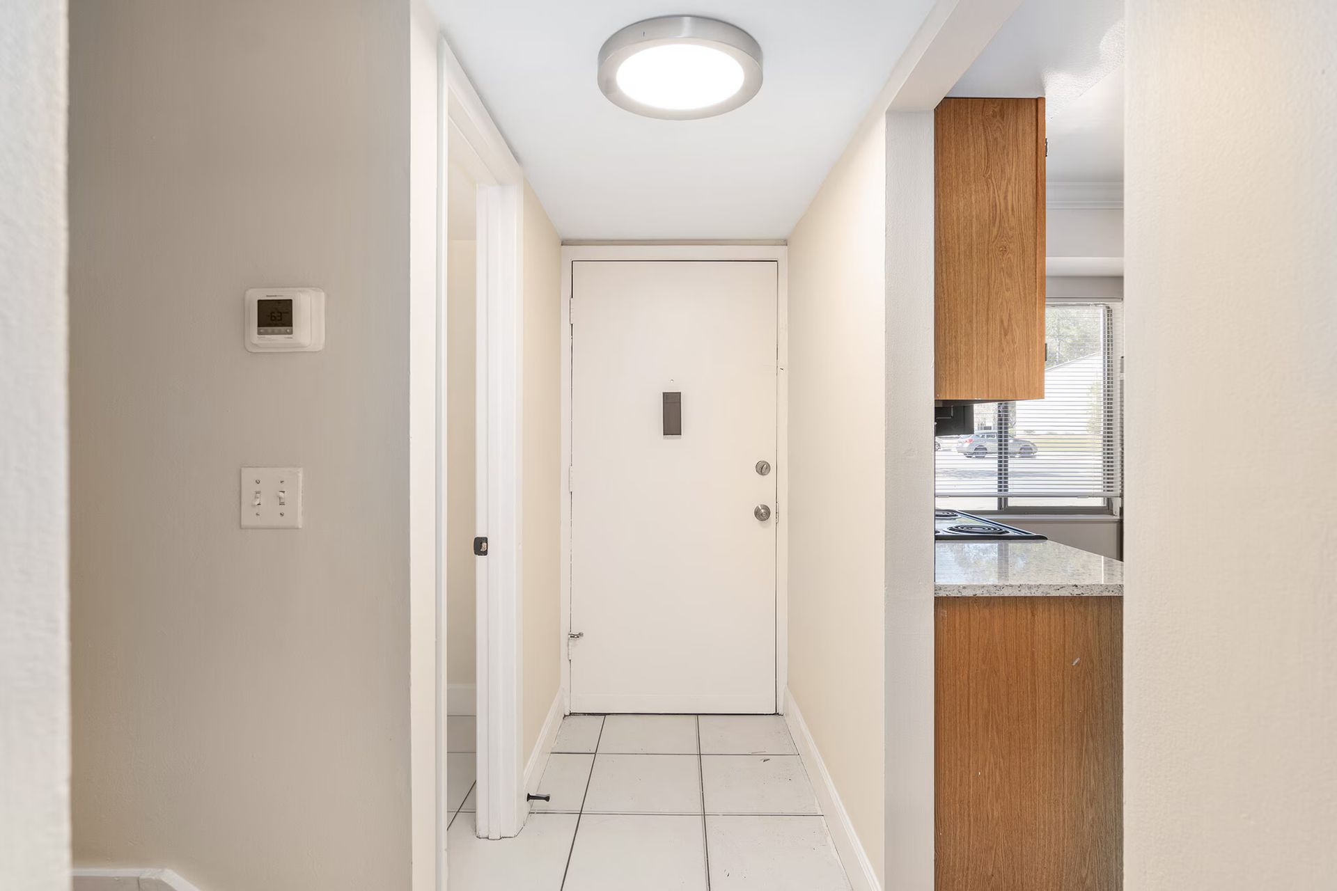 Hallway with white door, kitchen cabinets, and tile floor.