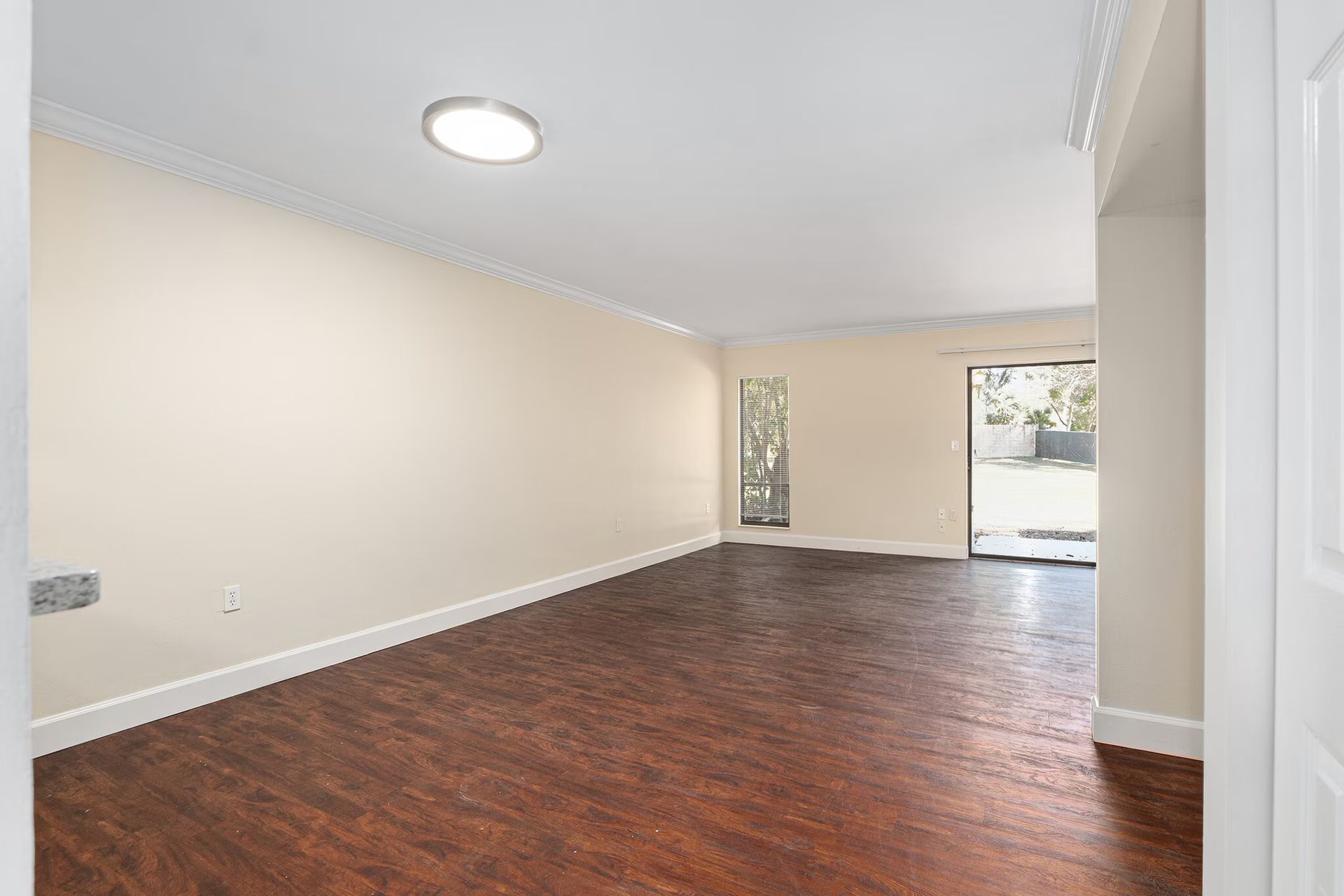 Empty living room with wood floors, white walls, and a sliding glass door to the outside.