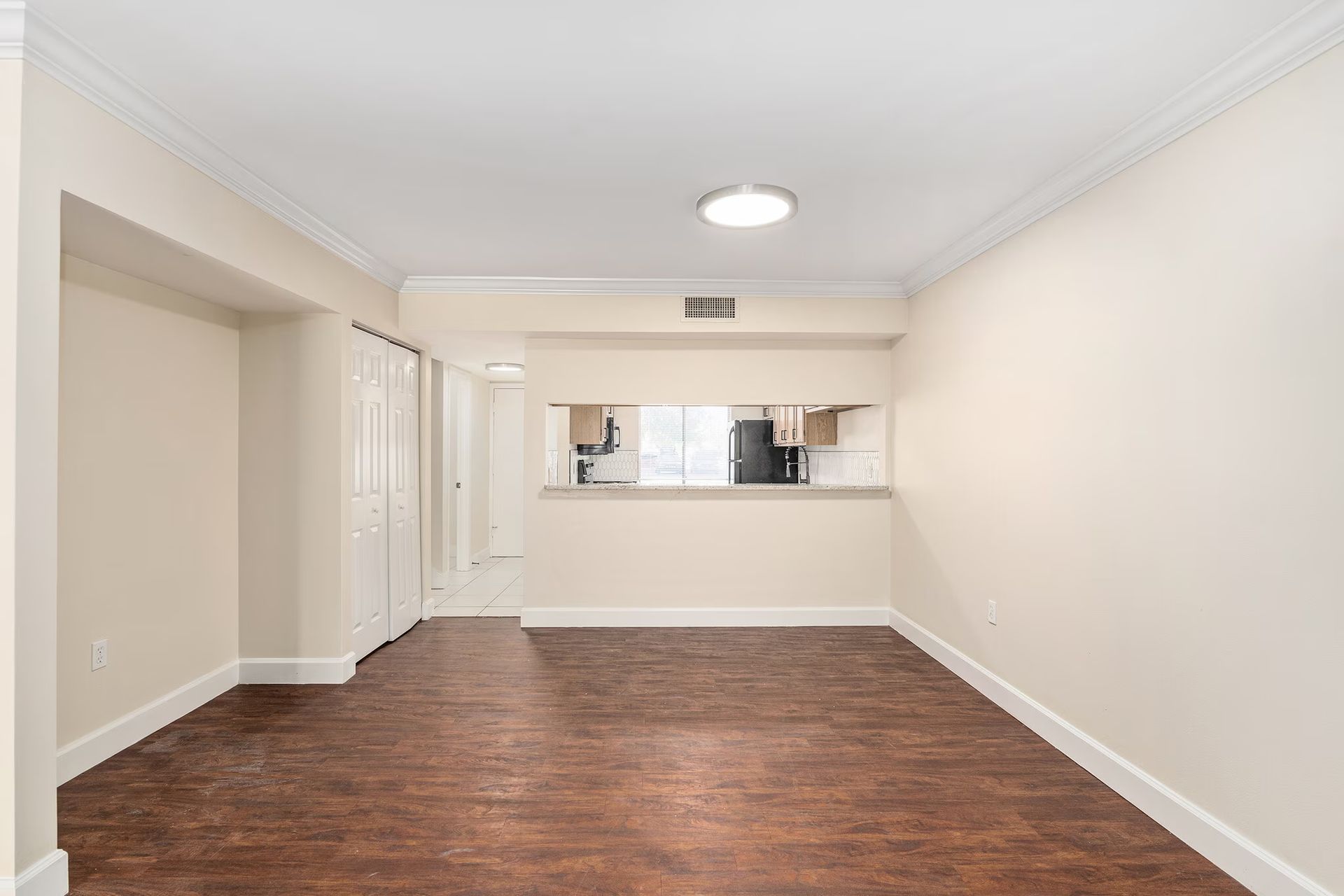 Empty living room with hardwood floors, opening to a kitchen, and light-colored walls.