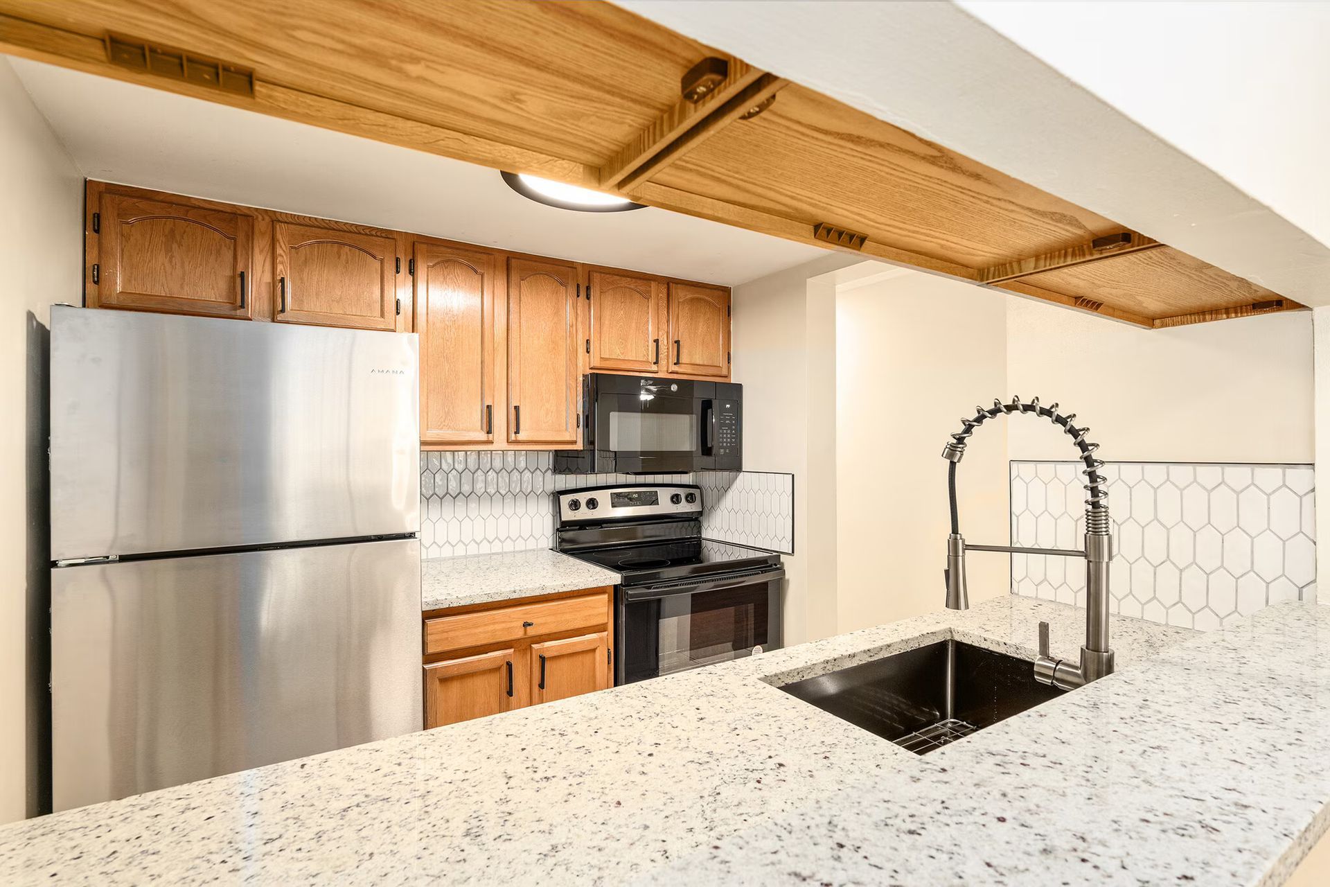 Kitchen with stainless steel refrigerator, stove, microwave, light wood cabinets, white countertop, black faucet.