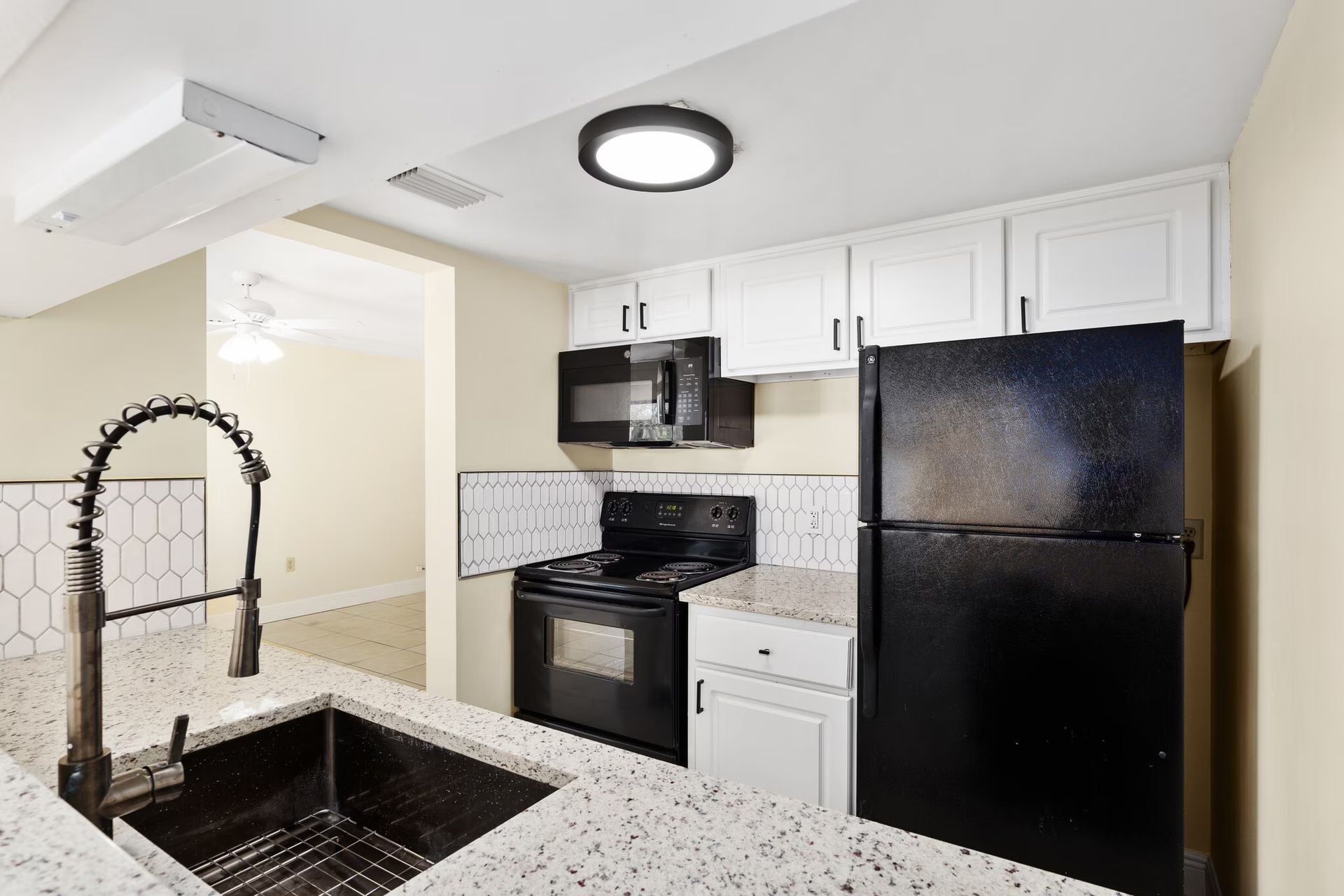 Modern kitchen with black appliances, white cabinets, and granite countertops.
