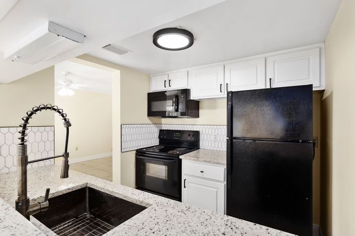 Modern kitchen with black appliances, white cabinets, and granite countertops.