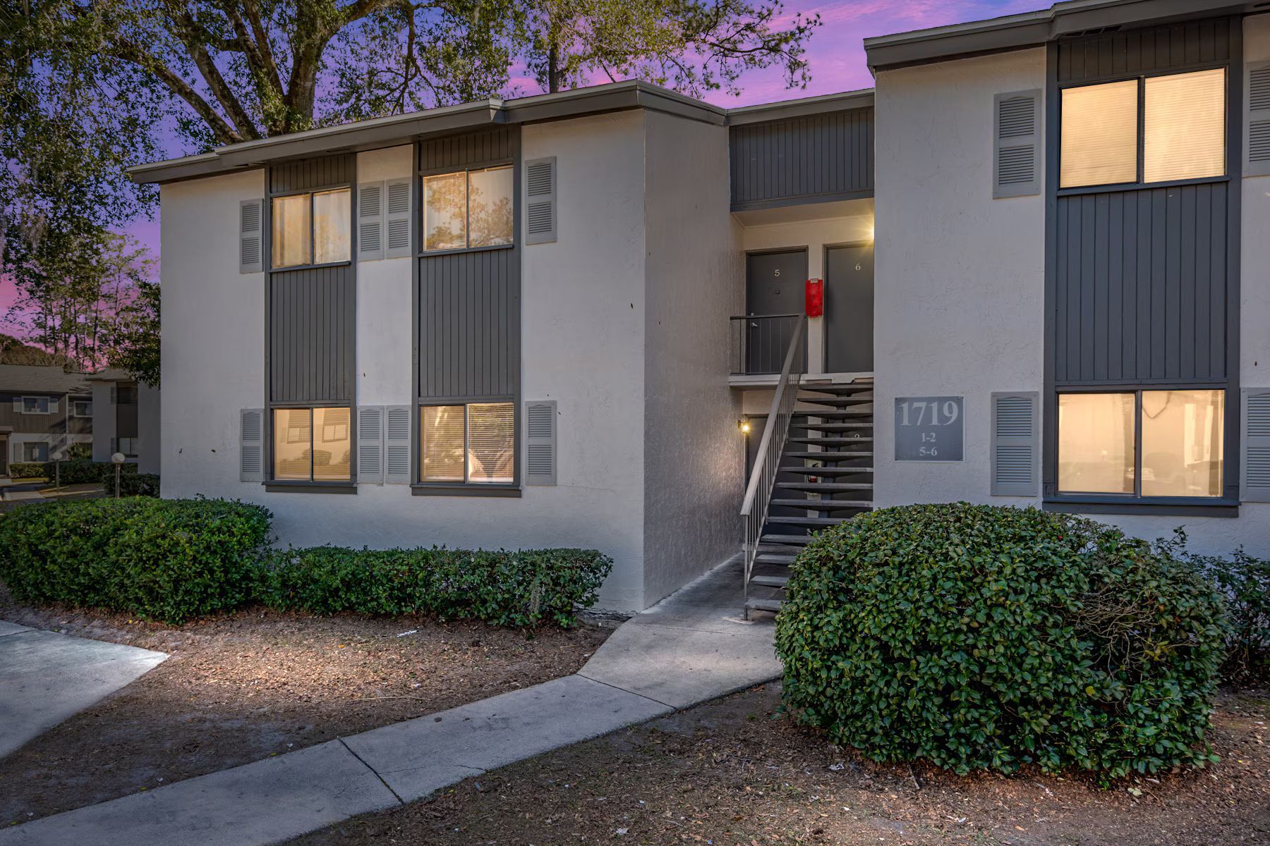Apartment building exterior with bushes and walkway; dusk sky.