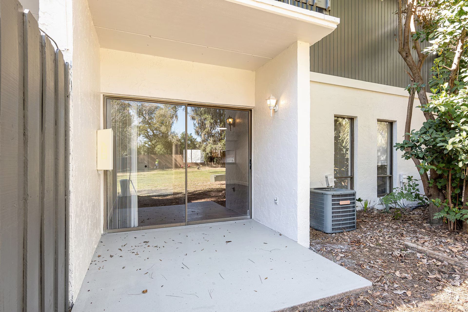 Patio with sliding glass doors, exterior view of a building with air conditioning unit.