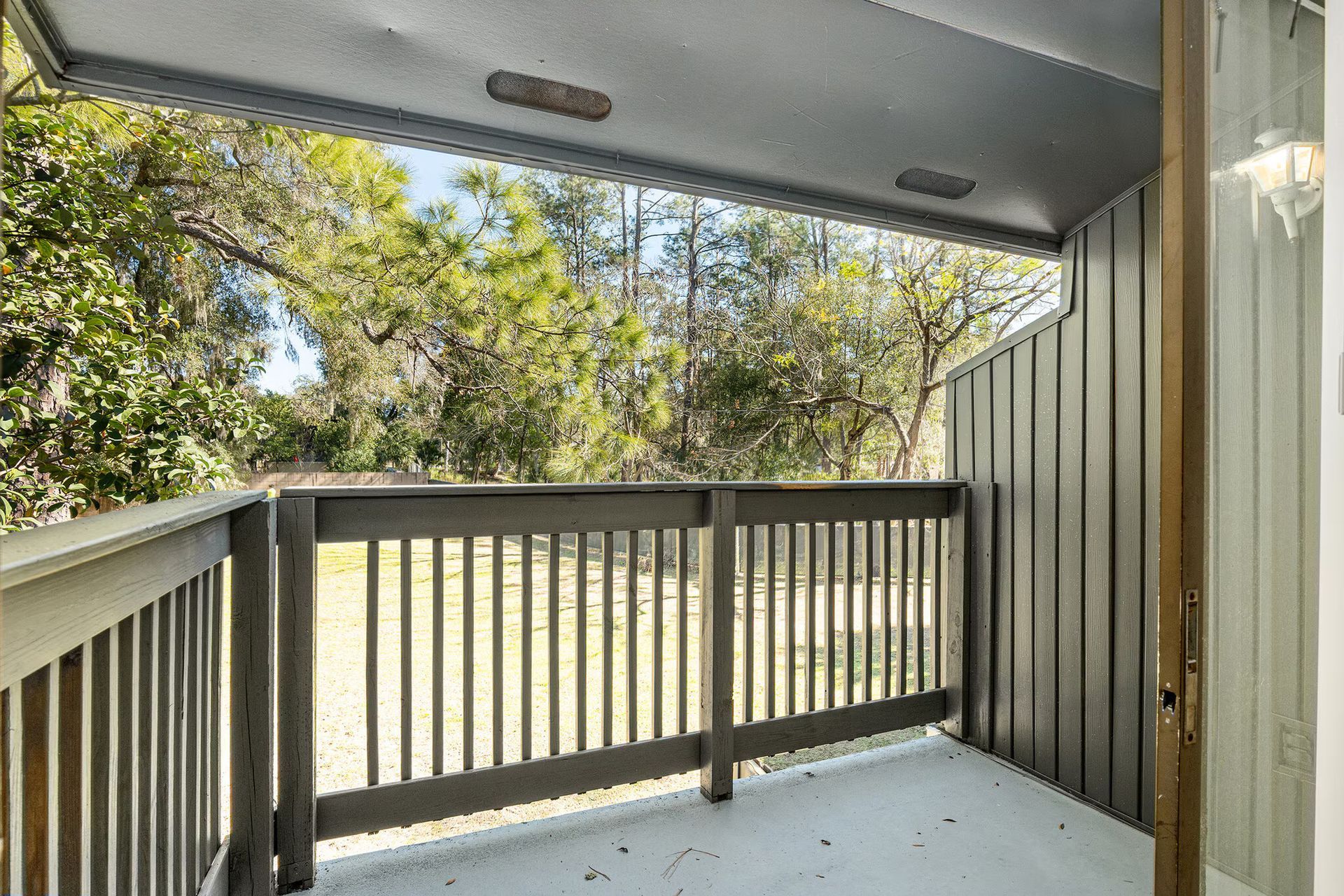 Balcony with wooden railing overlooking trees, bright daylight.