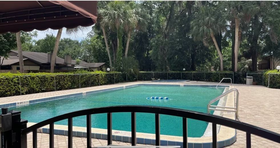 Swimming pool with wrought iron fence, surrounded by bushes and trees.