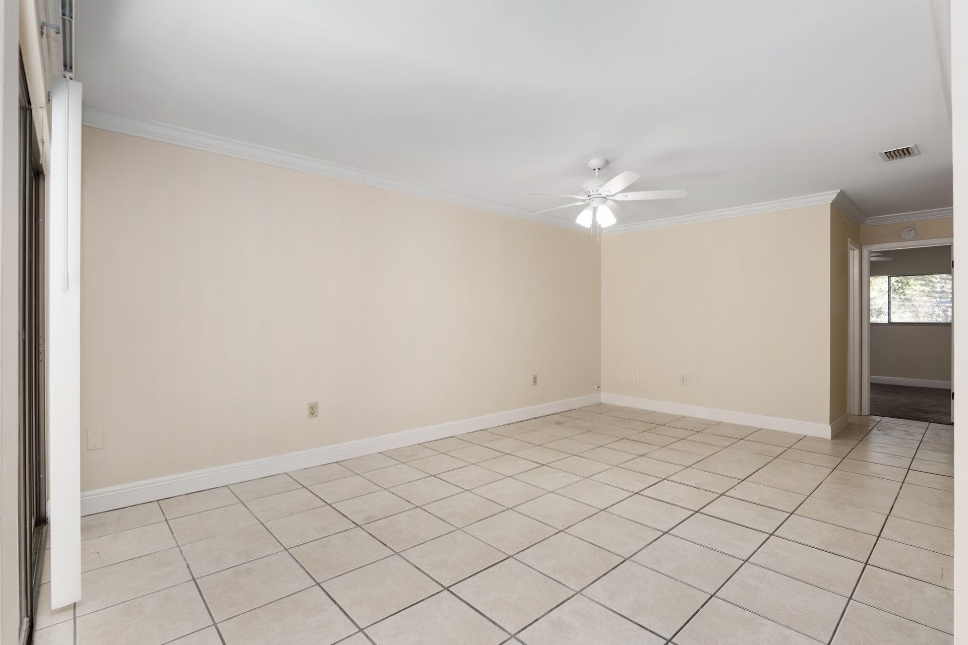 Empty room with tiled floor, beige walls, crown molding, and a ceiling fan.
