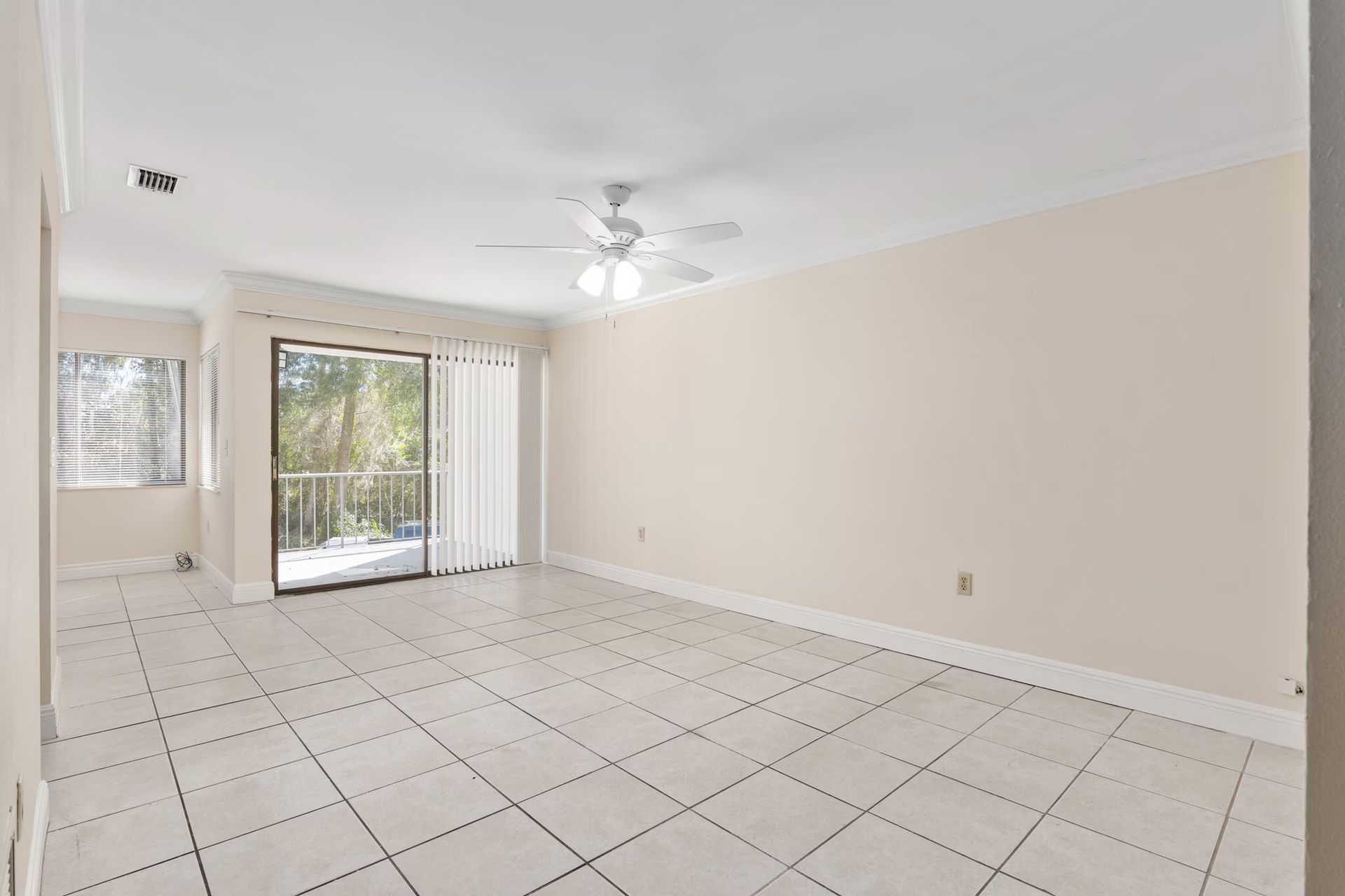 Empty living room with white tile floor, sliding door to balcony, ceiling fan, and neutral walls.
