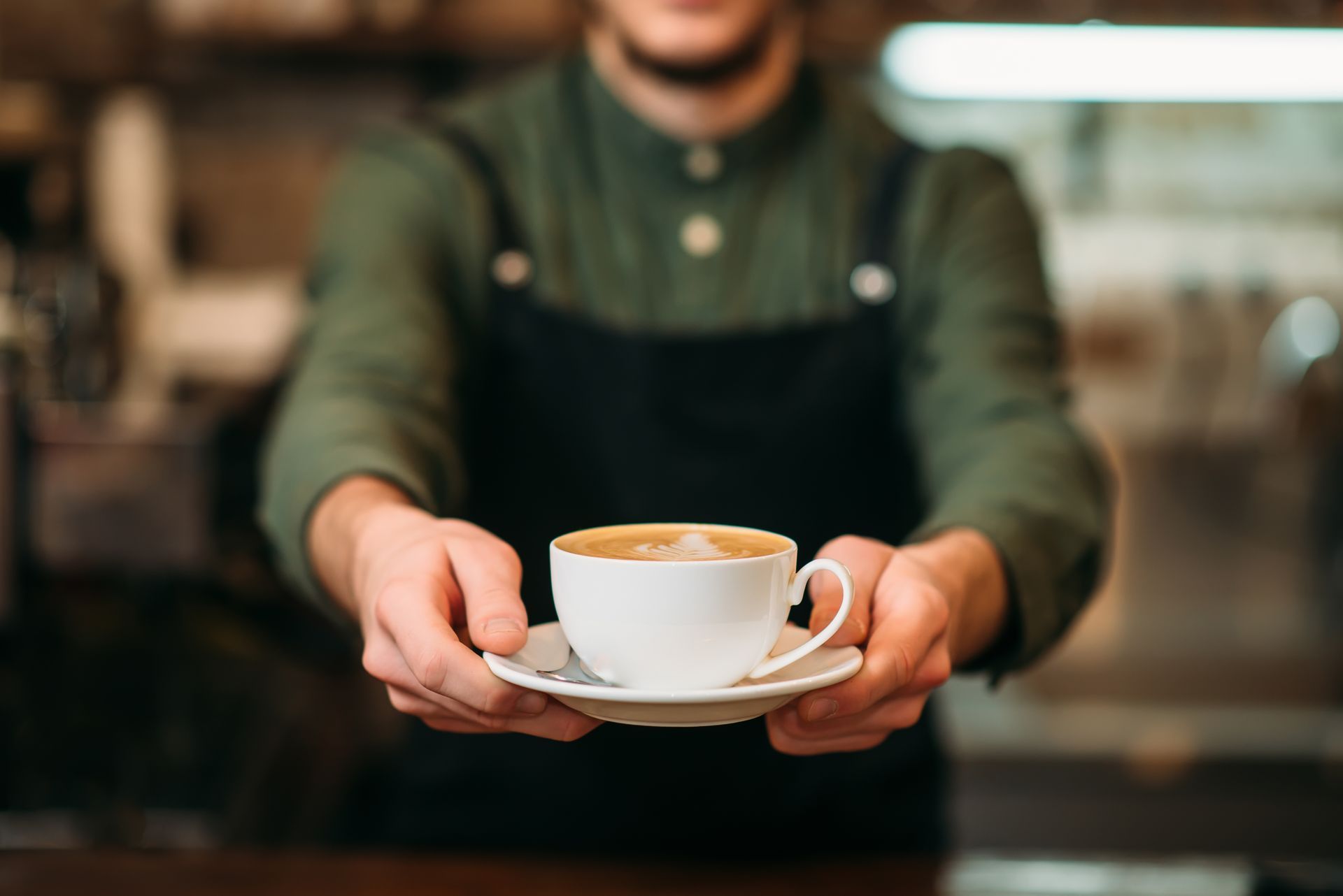 A barista is holding a cup of coffee in his hands.