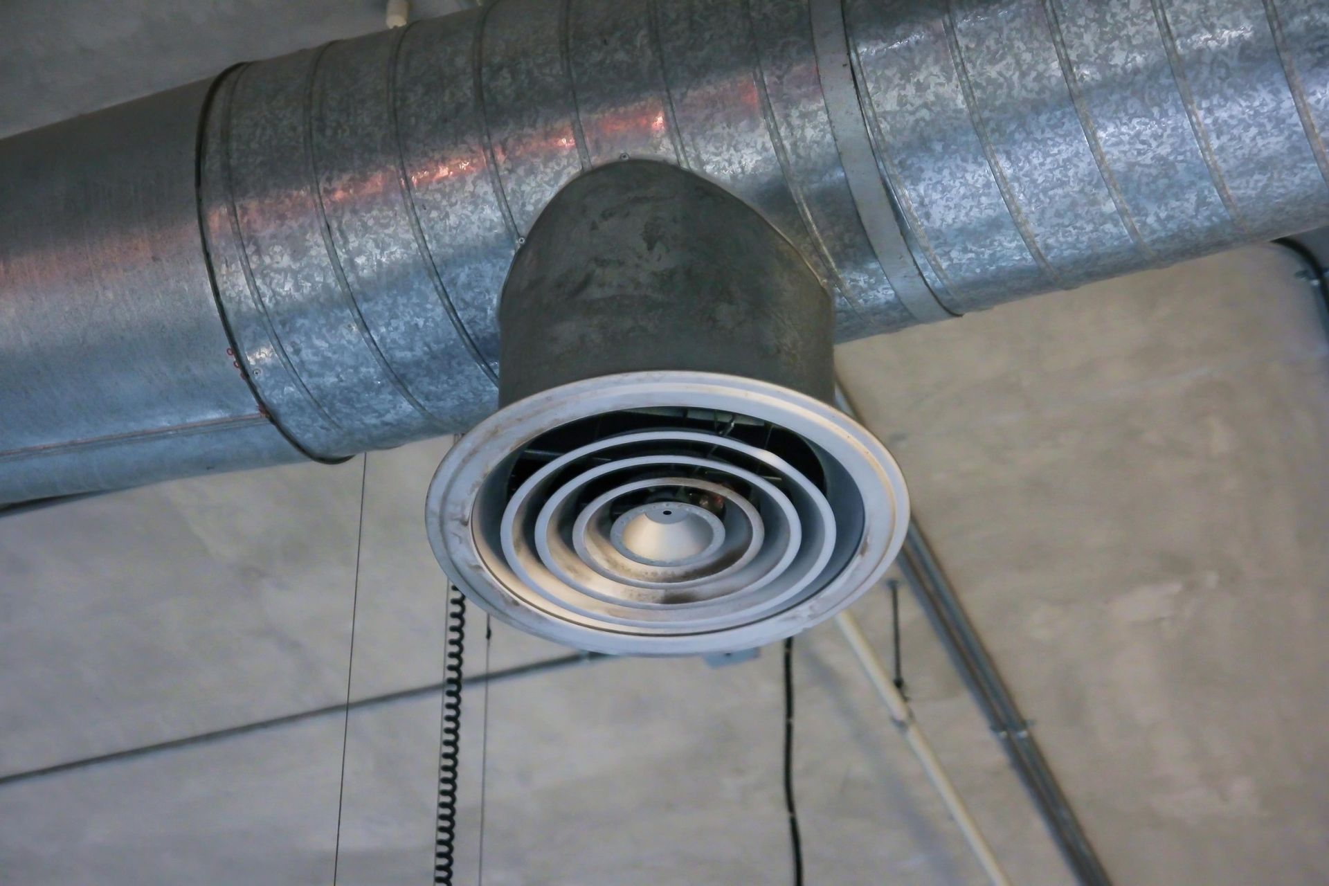 A metal pipe with a fan attached to it is hanging from the ceiling.