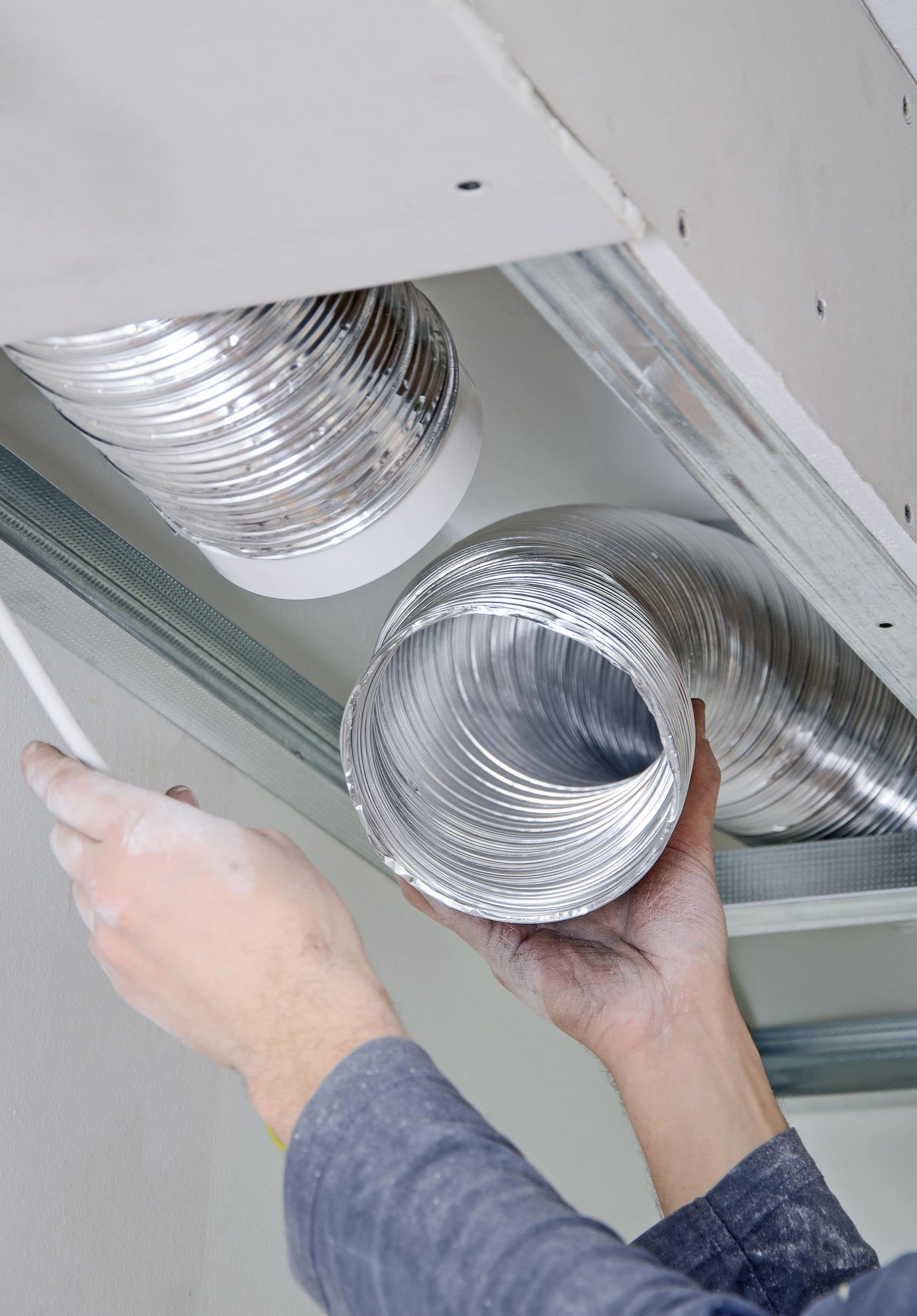 A person is holding aluminum ducts in their hands under a ceiling.