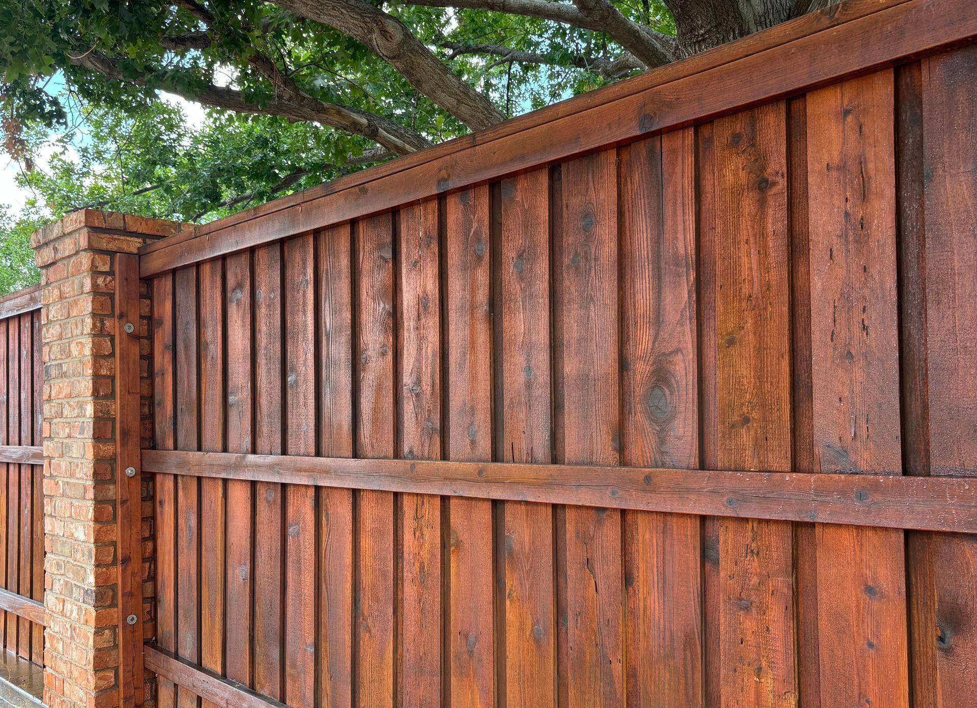 Wooden fence with brick pillar; stained reddish-brown.
