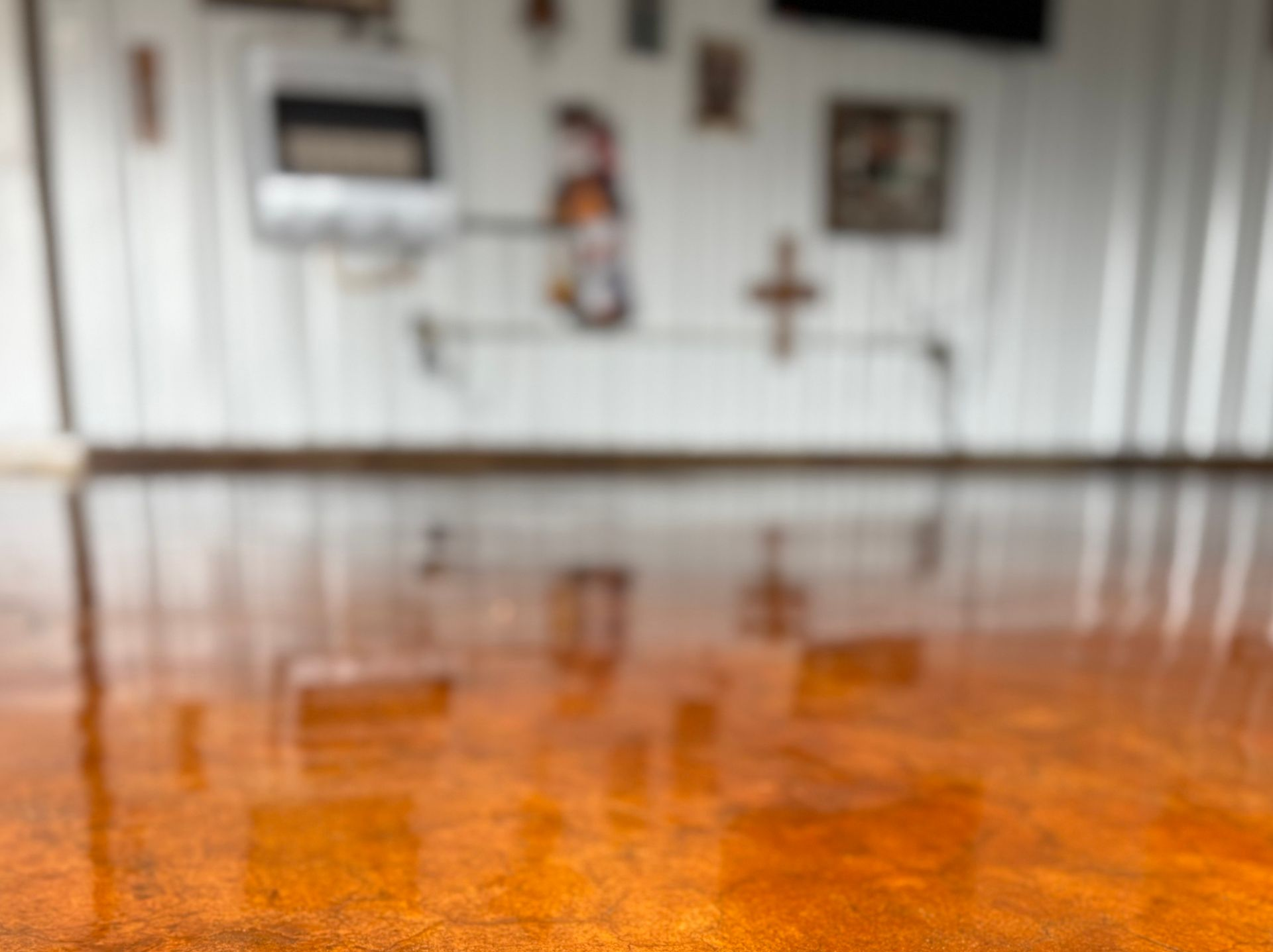Shiny orange epoxy floor reflecting a blurred interior with decorative objects on a white wall.