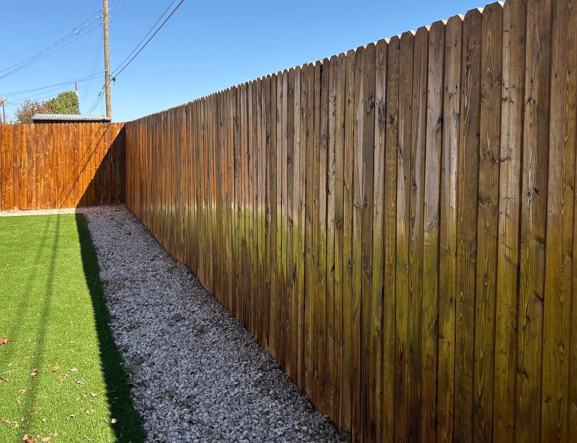 Wooden fence along a gravel path and green grass under a clear, blue sky.