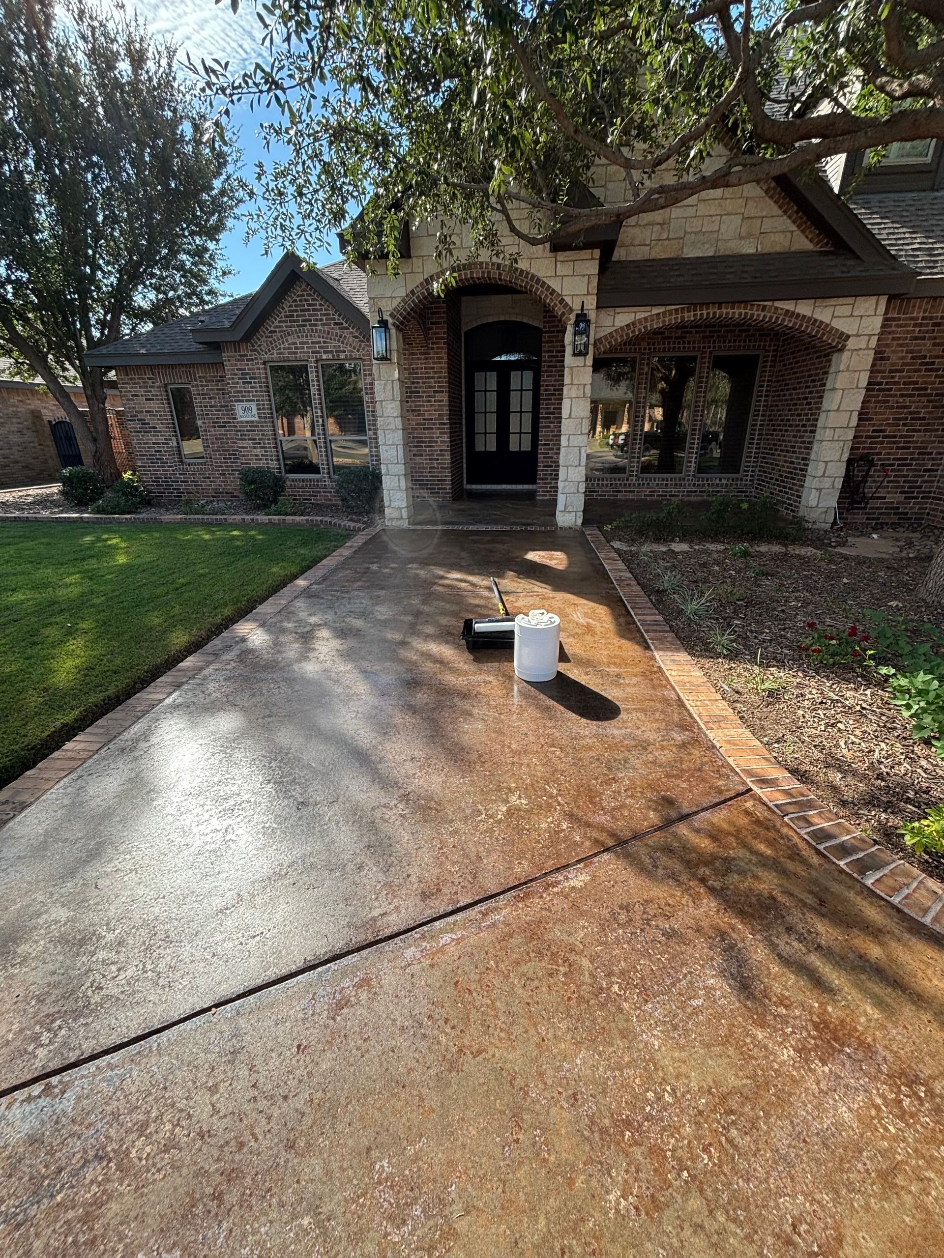 Concrete driveway leading to a brick house with a person's painting supplies in front of the entrance.