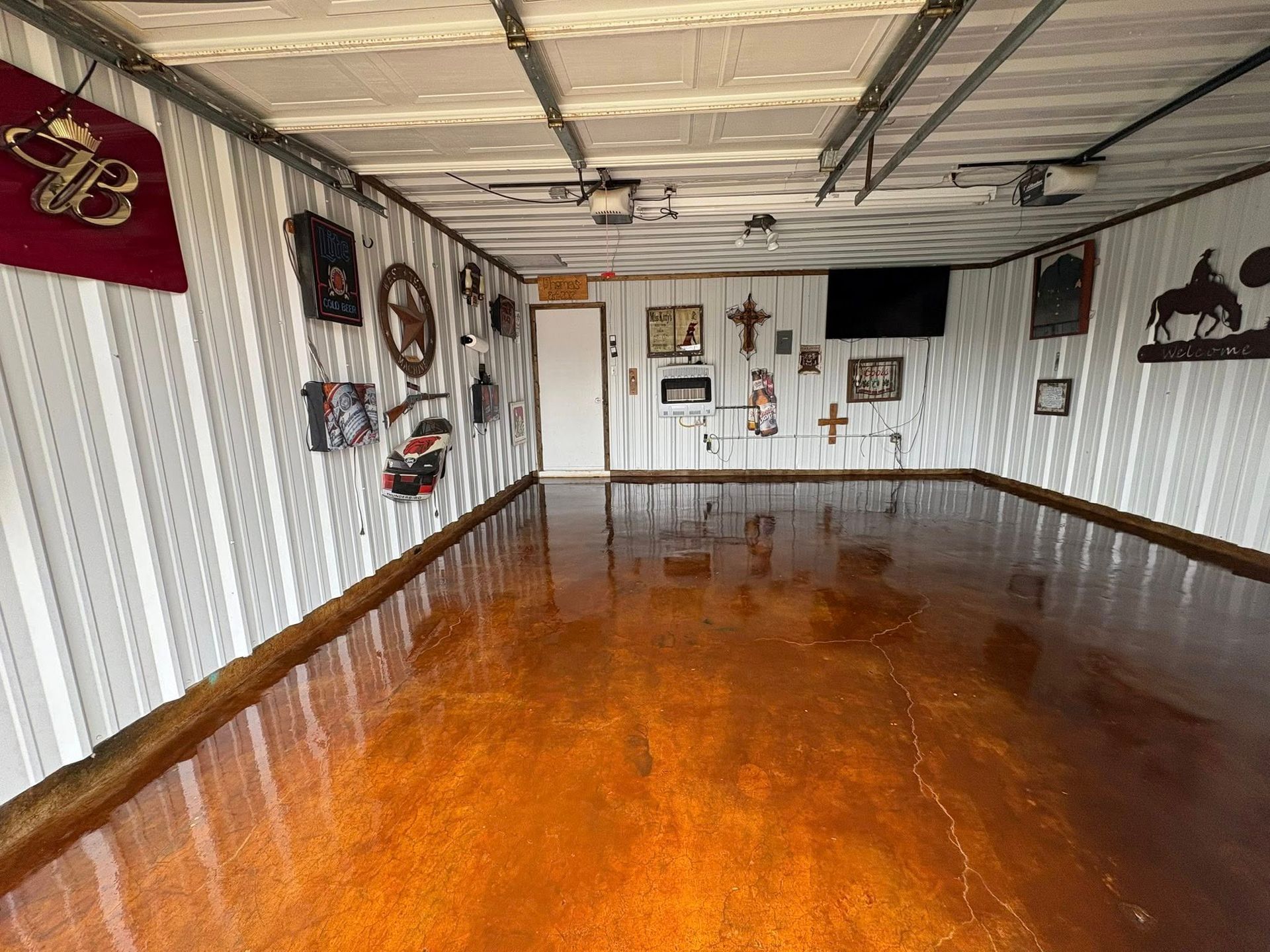 Garage with shiny, copper-colored floor, white-striped walls, decorated with western art and bar sign.