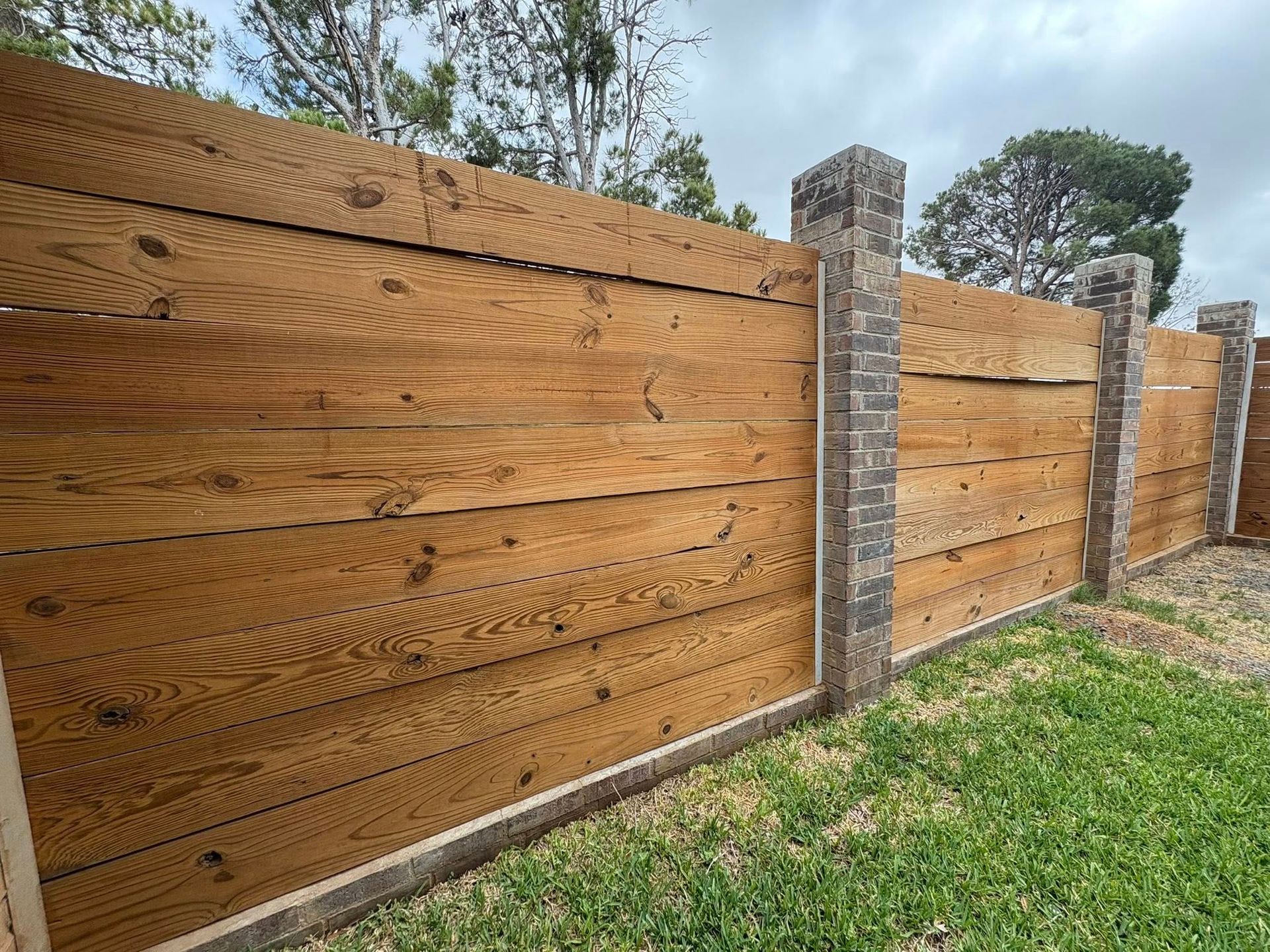 Wooden fence with brick pillars; set in a grassy yard under a cloudy sky.