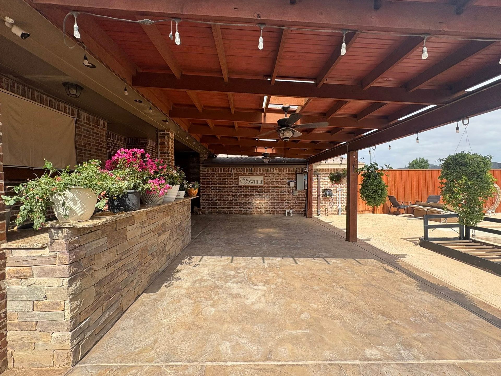Covered patio with brick and stone accents, ceiling fan, and string lights.