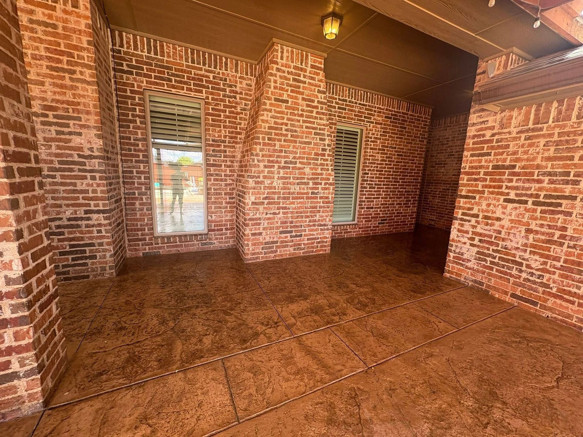 Brick-walled patio with stamped concrete flooring. Two windows and a light fixture visible.