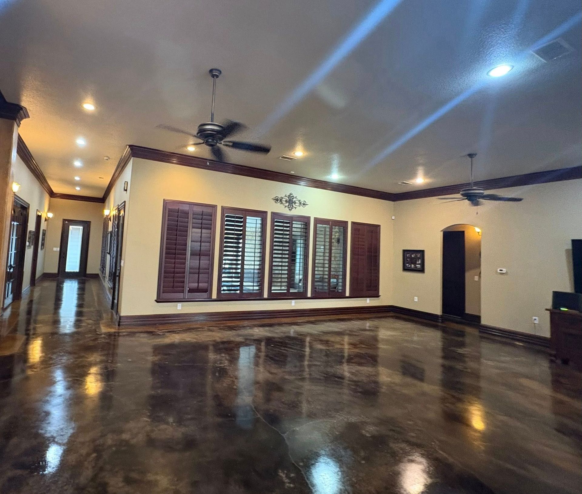 Spacious room with shiny brown floor, brown shutters, and two ceiling fans.