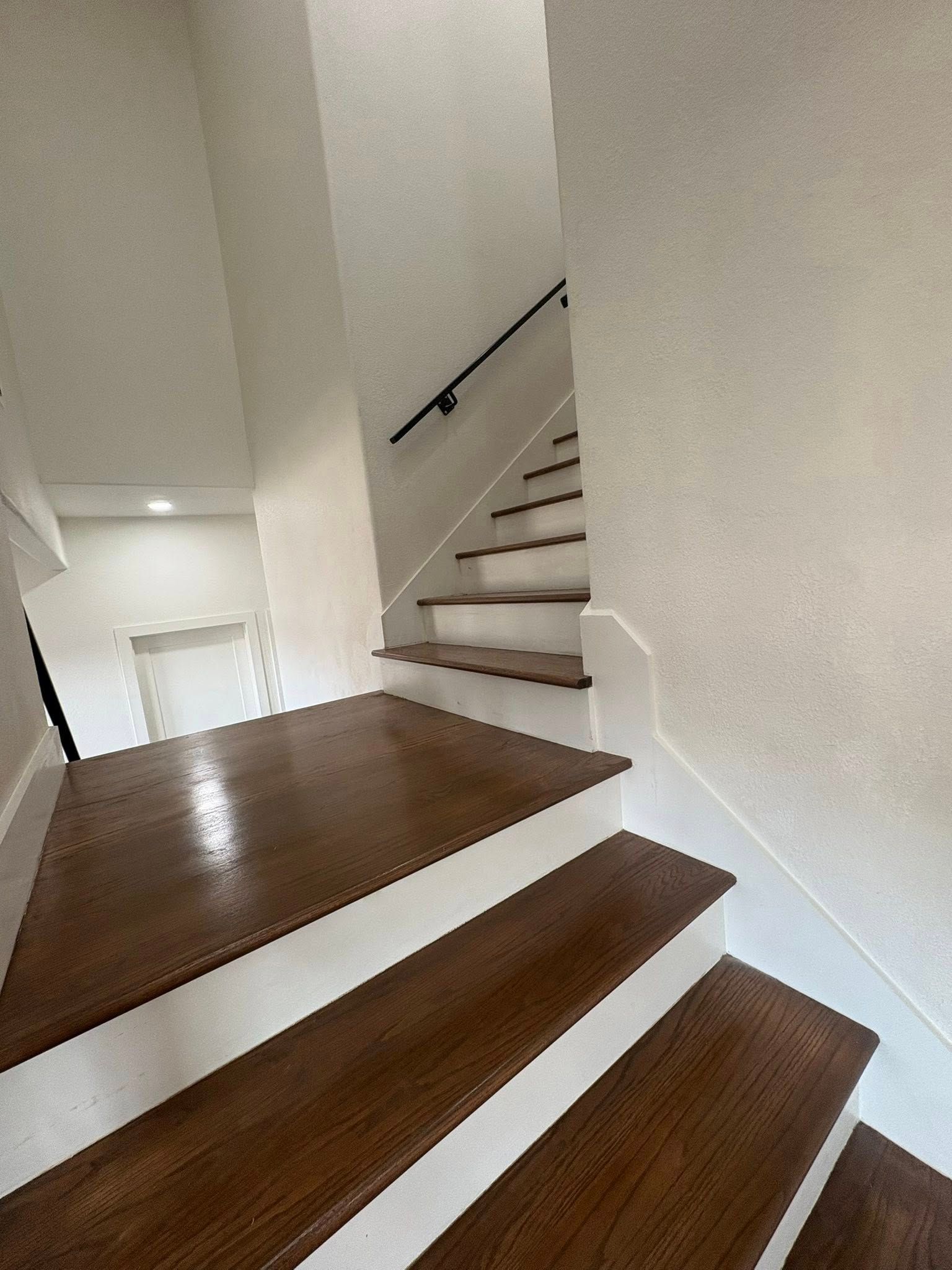 Wooden staircase with white risers and dark wood treads; a black handrail on the right.