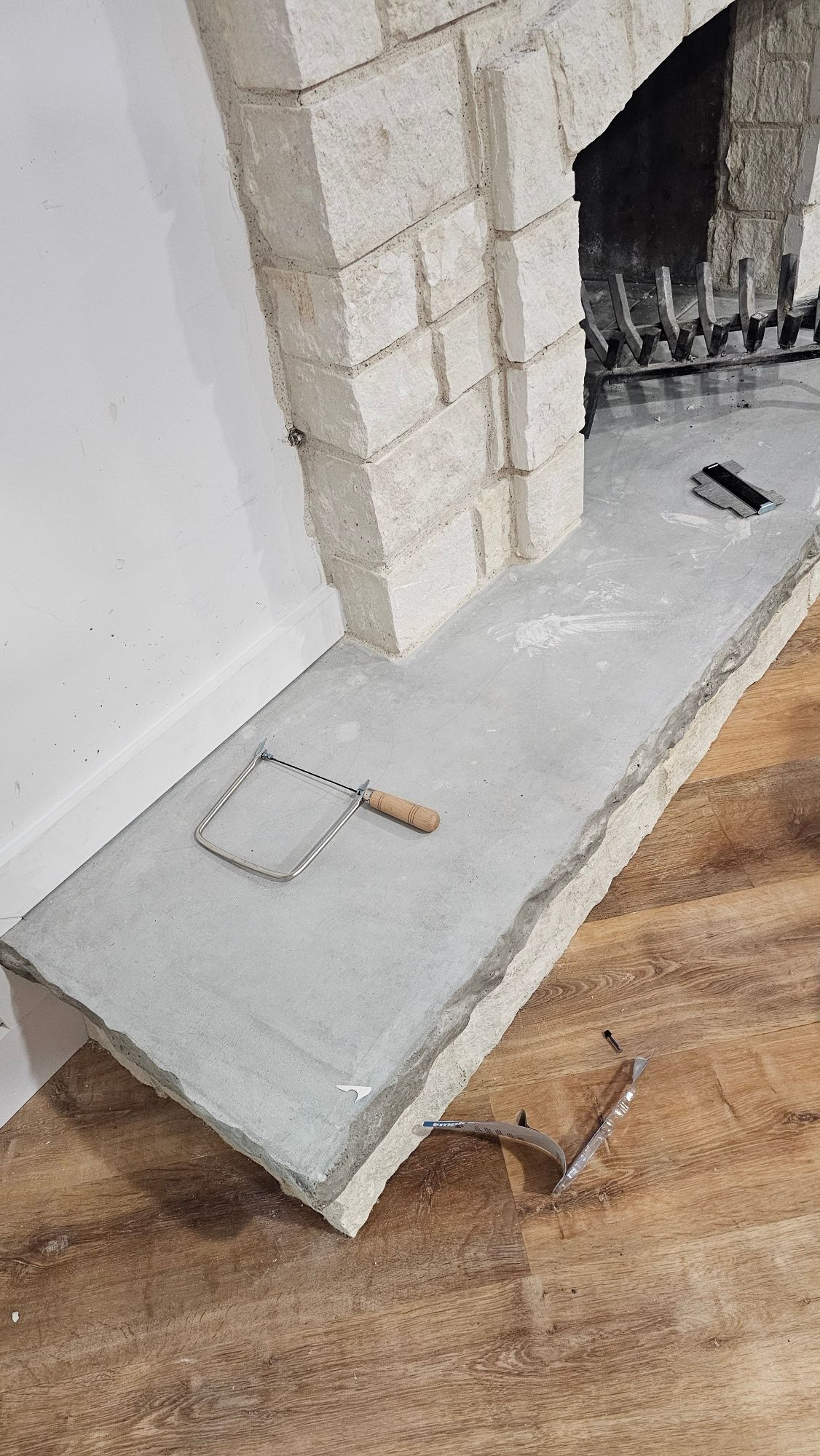 A partially constructed fireplace hearth with a saw and tools on a concrete surface.