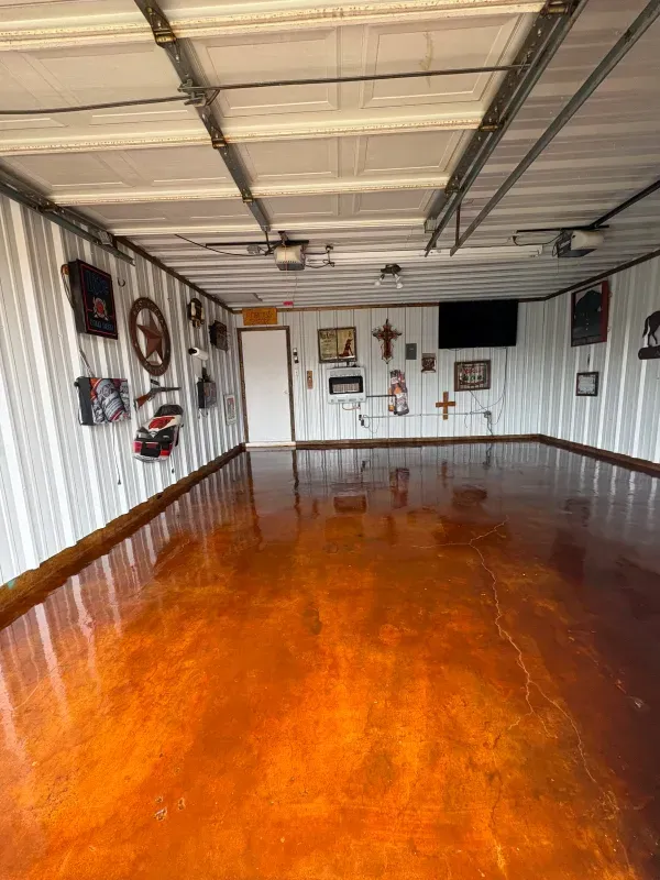 Inside a garage: polished orange floor, white walls, decorative items, overhead lights, closed white door, a mounted TV.