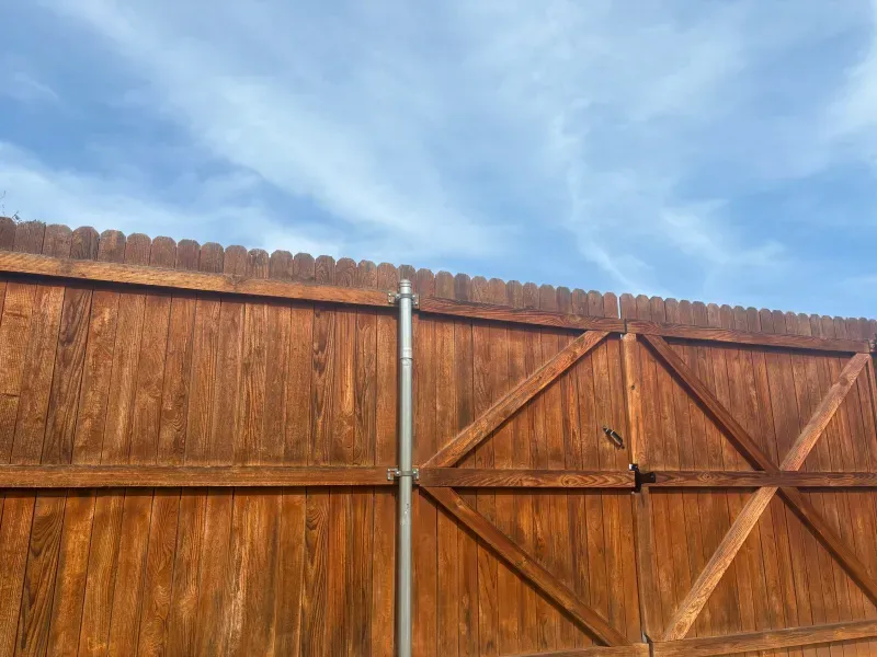 Brown wooden fence with a sky blue background. A vertical metal pole is attached to the fence.
