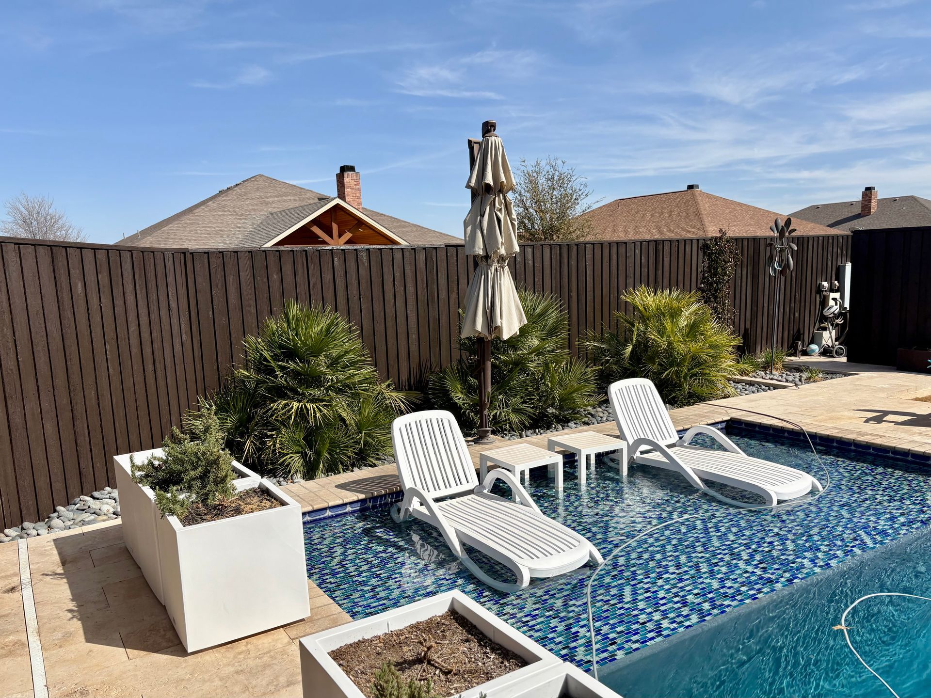 Swimming pool with lounge chairs, umbrella, and a brown fence on a sunny day.